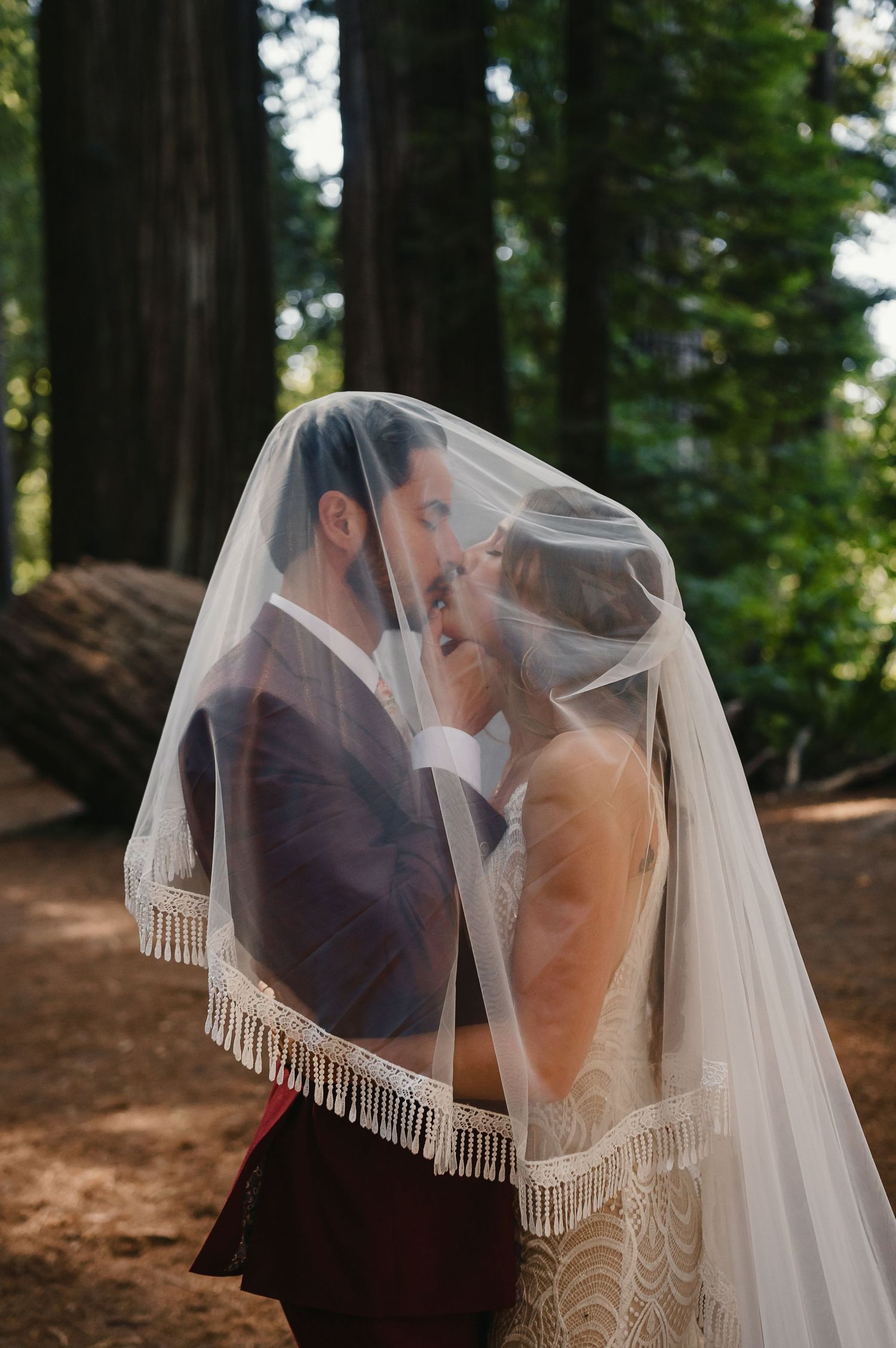 A couple shares an intimate moment under a flowing veil in a peaceful forest setting.