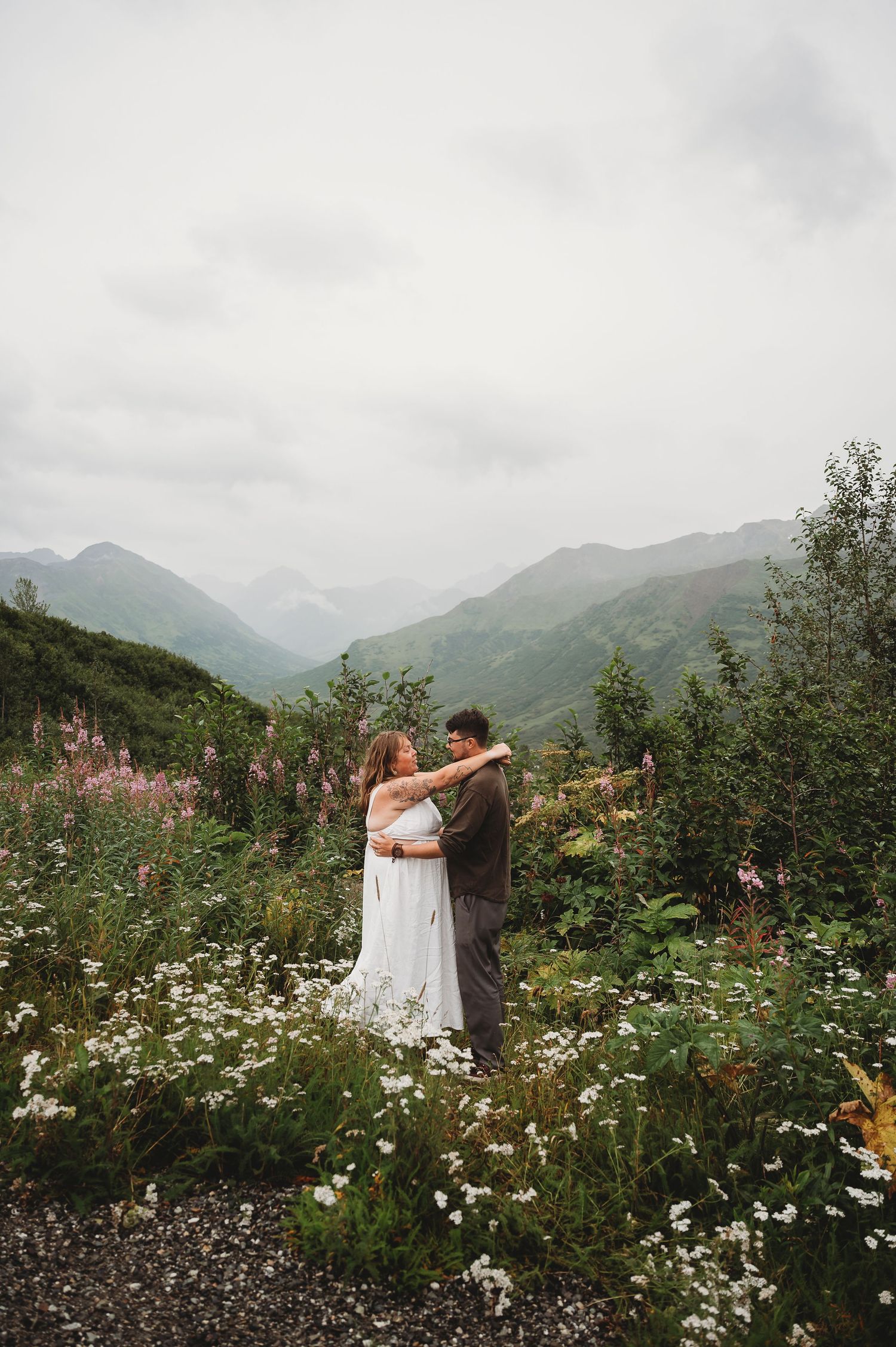 A couple embraces in a wildflower meadow with misty mountains in the background.