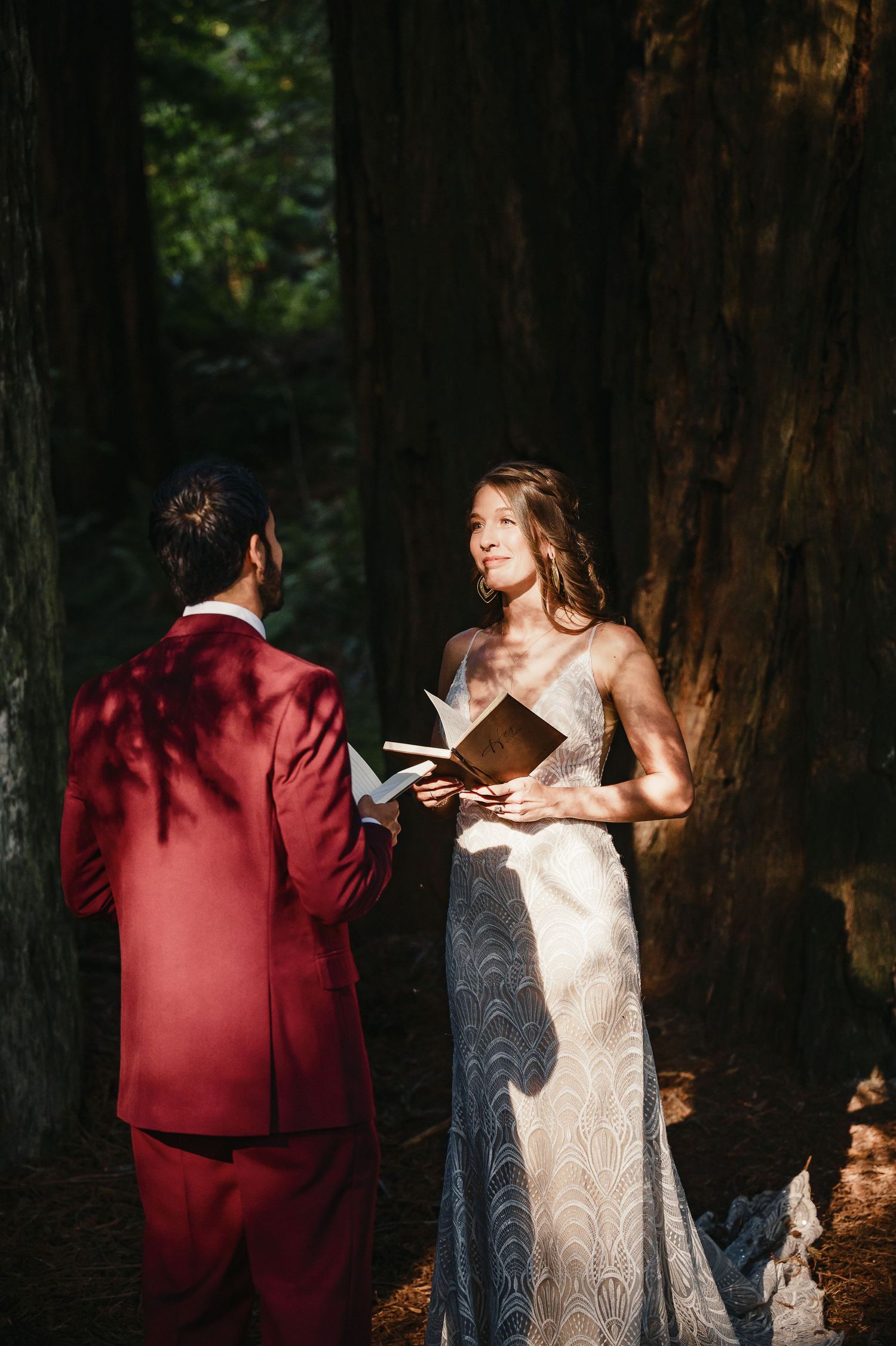 A couple exchanges vows in a lush forest setting, with sunlight filtering through tall trees.