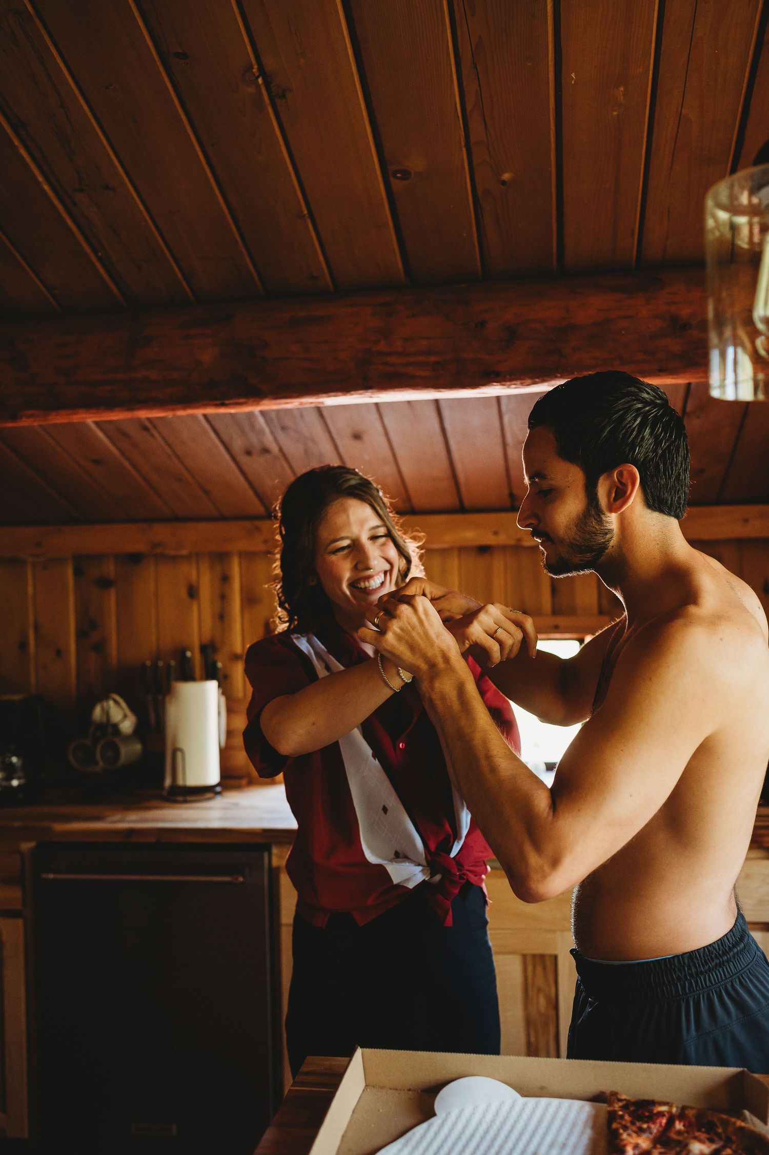 Wedding party members getting dressed and helping each other prepare in a wooden cabin.