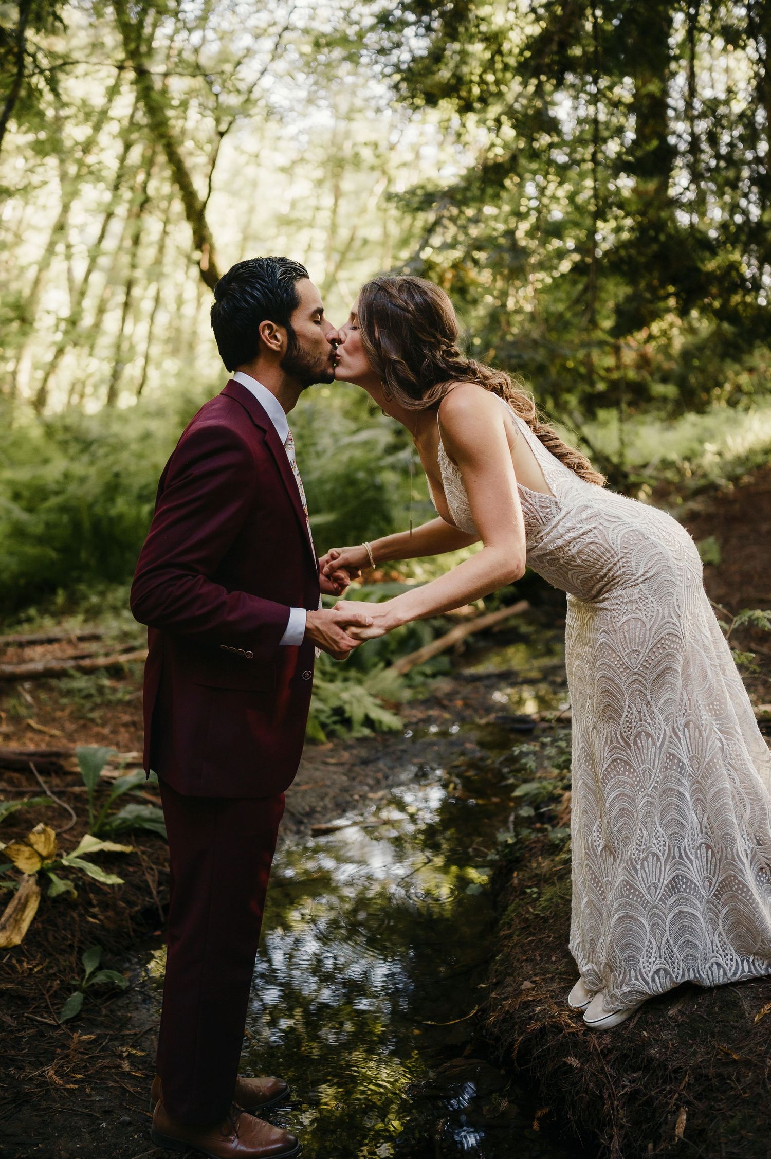 Couple sharing a tender moment by a stream in a magical forest setting.