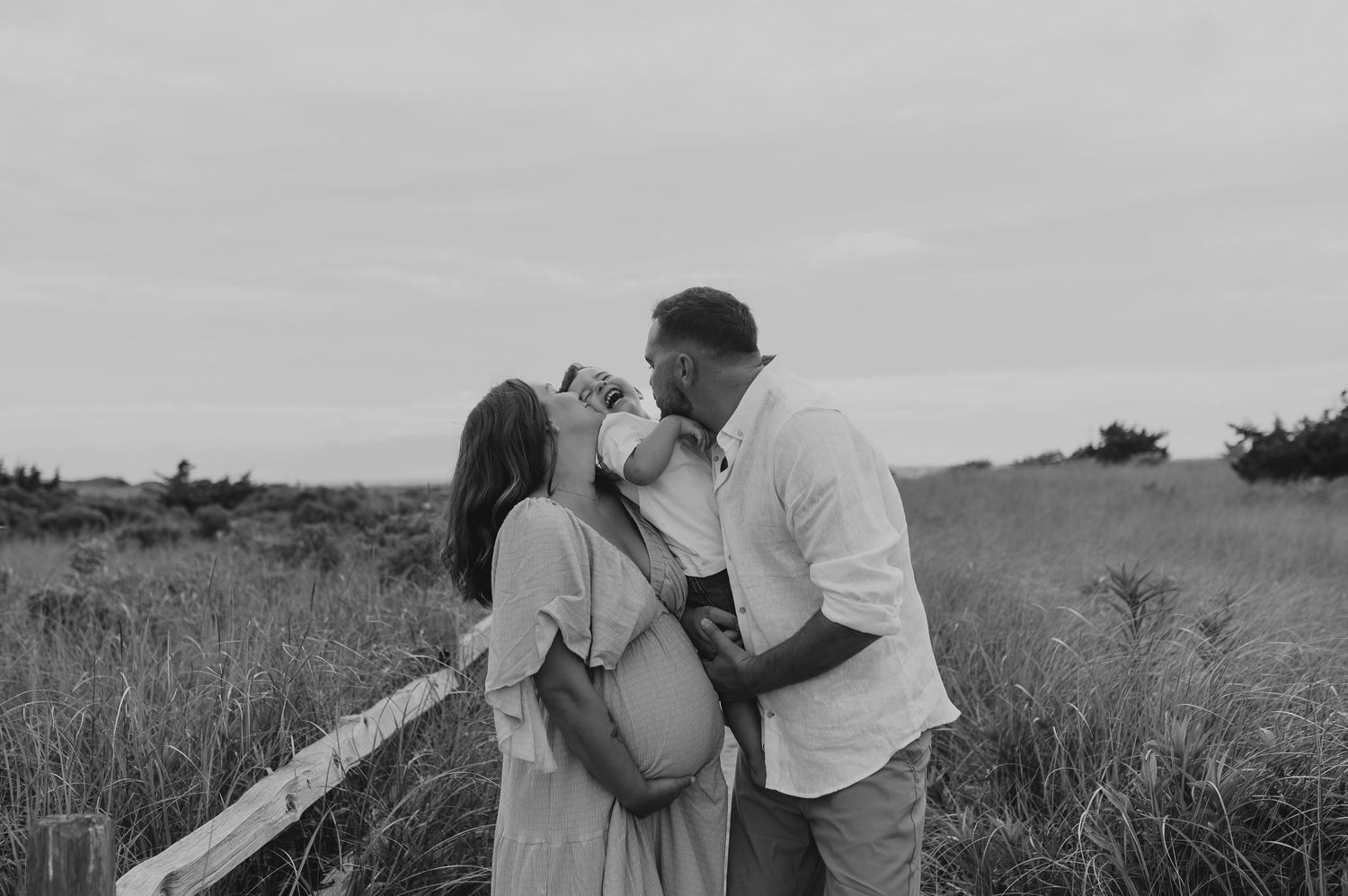 Black and white photo of couple embracing in a rustic field setting.