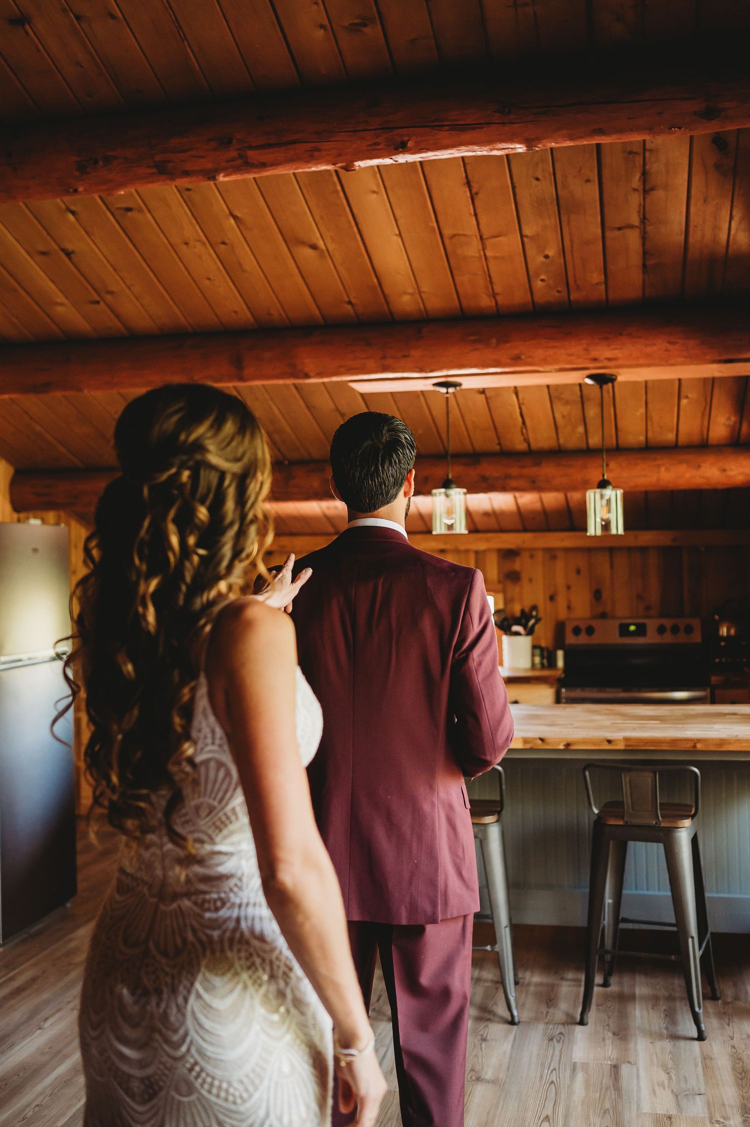A couple stands together under rustic wooden beams in a barn venue with moody lighting and industrial decor.