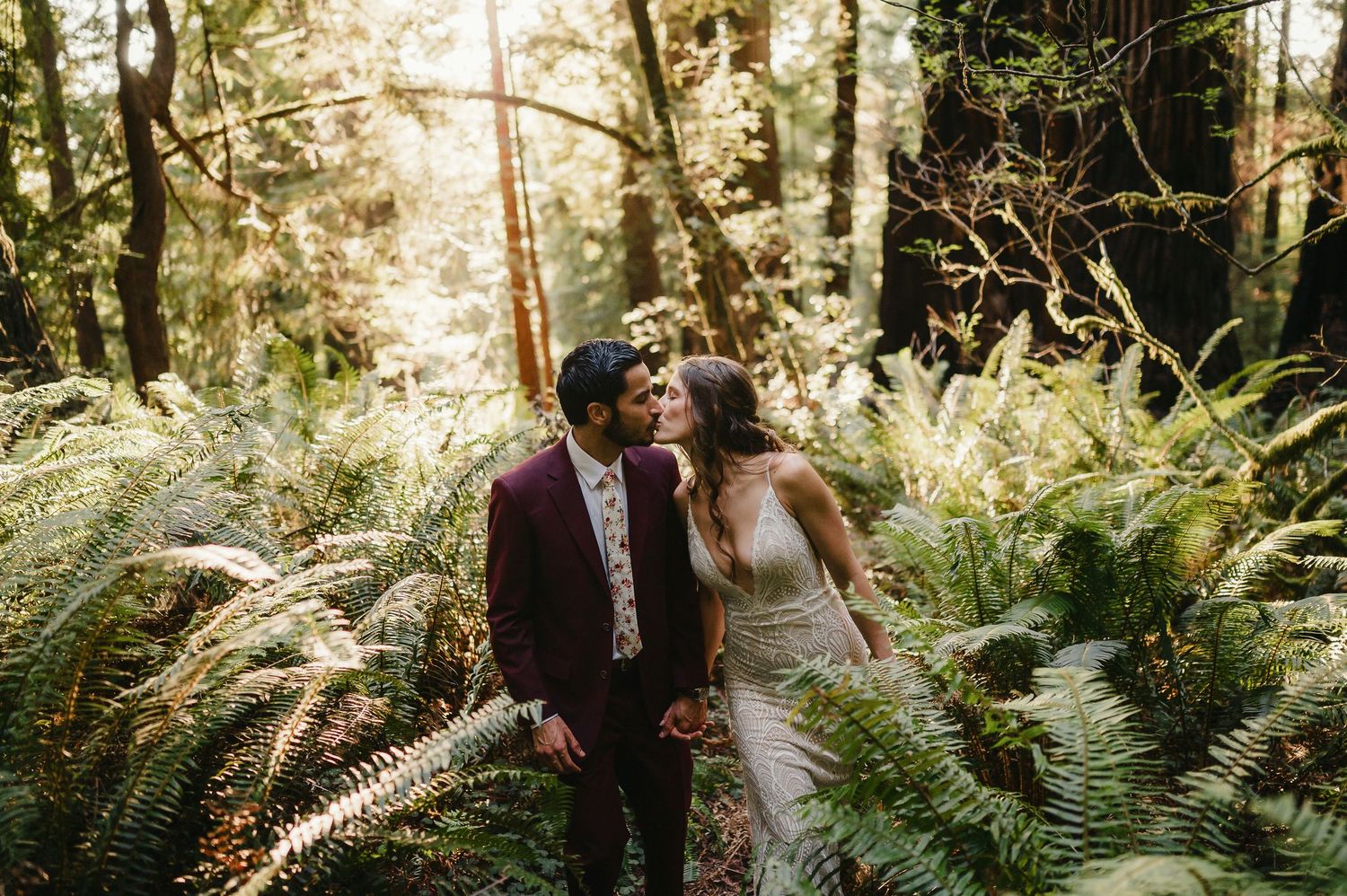 Romantic couple walks through a sunlit forest with tall trees and ferns in Vancouver Island.