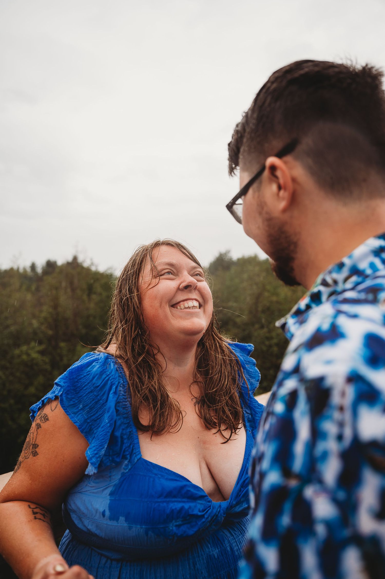 A joyful moment between two people outdoors on a cloudy day, one wearing a bright blue dress and the other in a patterned shirt.