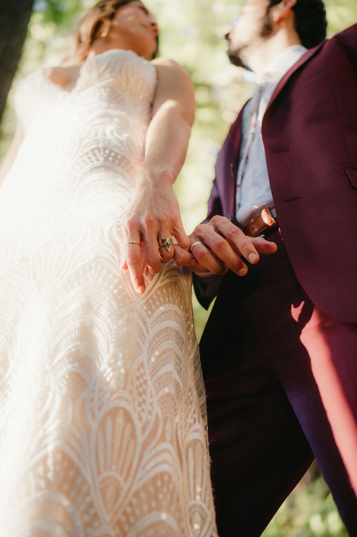 Close up detail of couple's hands with intricate lace wedding dress pattern in soft natural light.