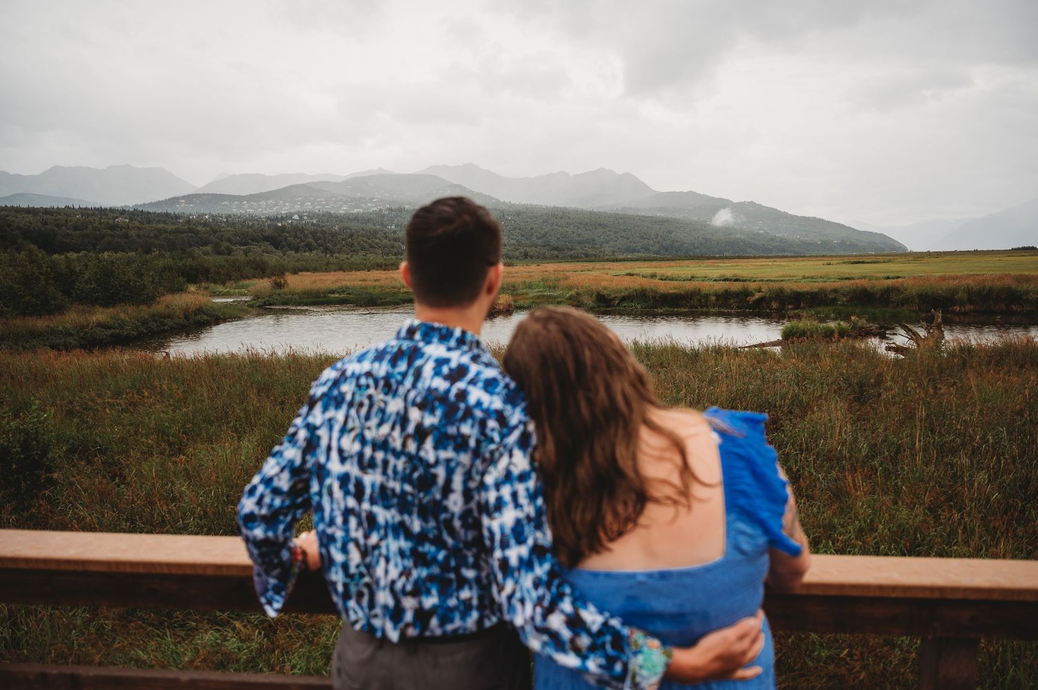 Two people in matching outfits embracing while looking out over a scenic mountain landscape.