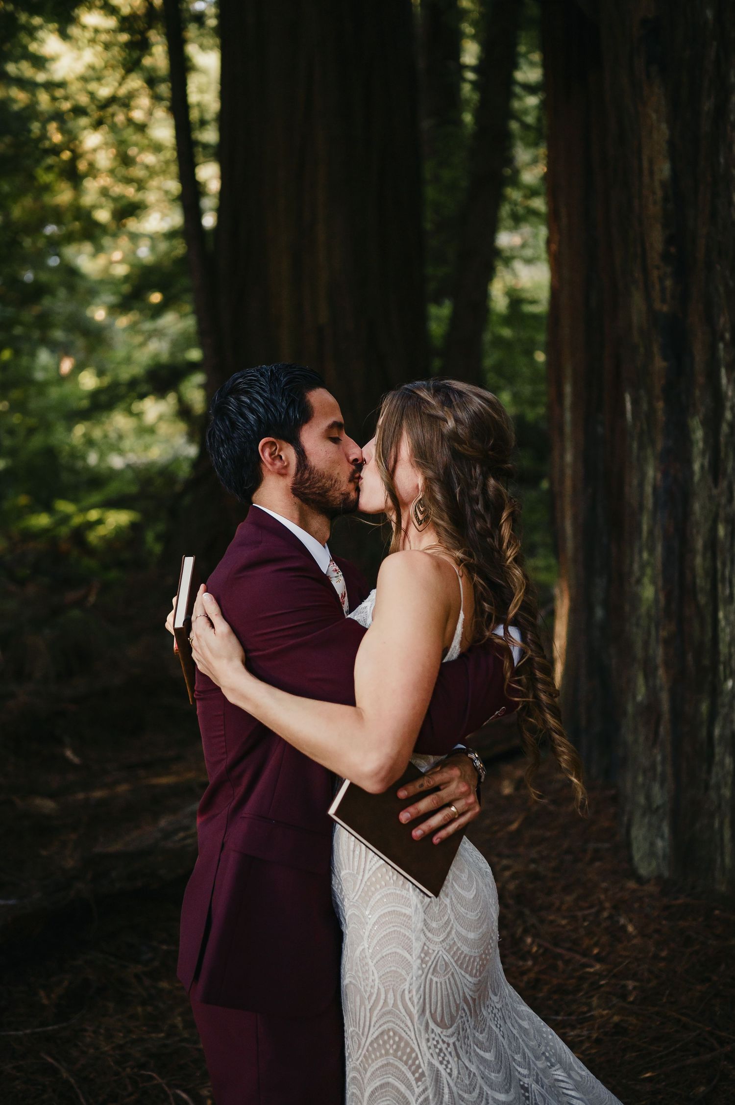 A romantic wedding couple shares an intimate kiss in a forest of tall redwood trees on their special day.