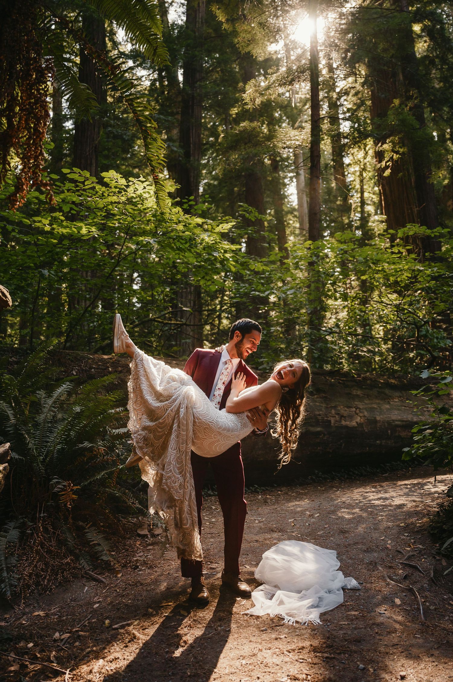 A romantic dance pose captured in a sunlit forest with flowing white dress and dramatic backlighting.