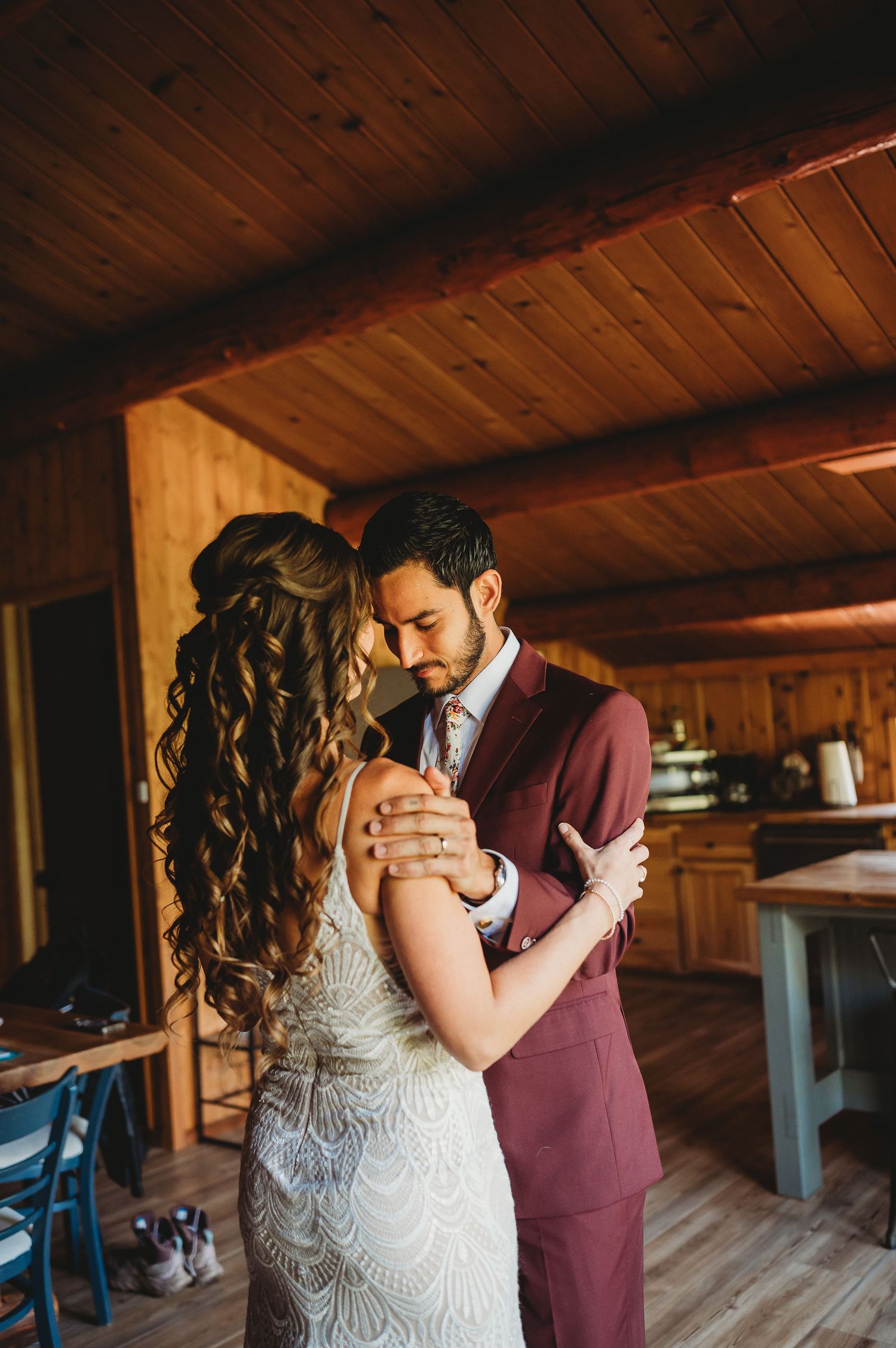Intimate wedding first look between couple in burgundy suit and lace dress inside wooden cabin.