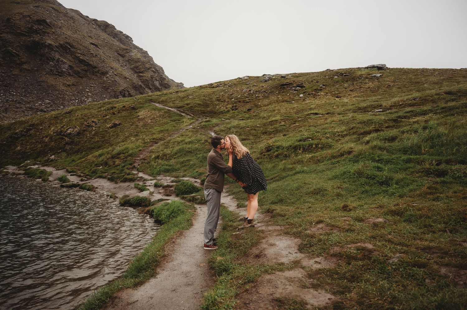 Two people walking along a mountain trail surrounded by rugged alpine terrain.