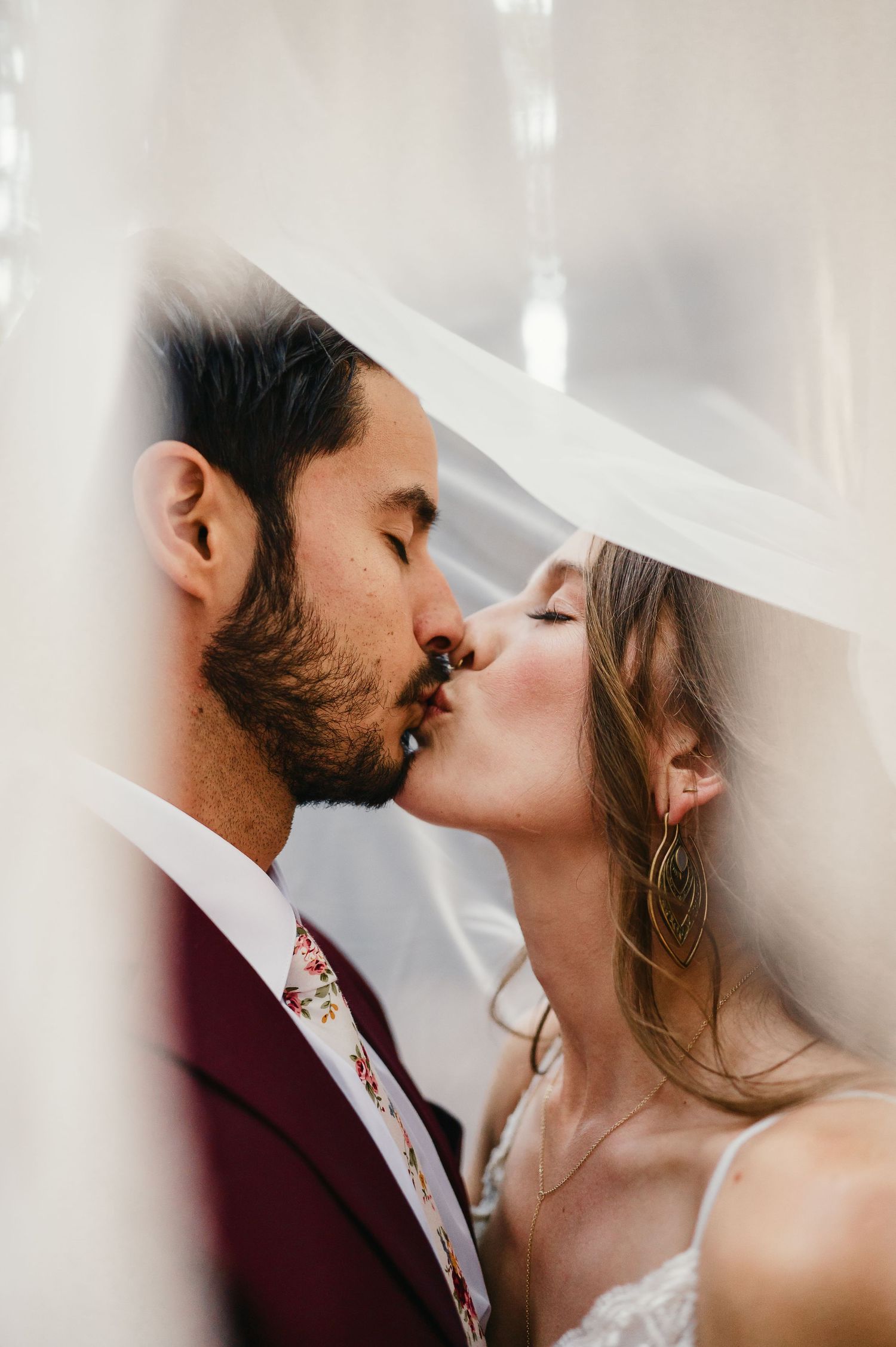 Intimate wedding couple portrait with delicate veil creating soft romantic lighting effects.