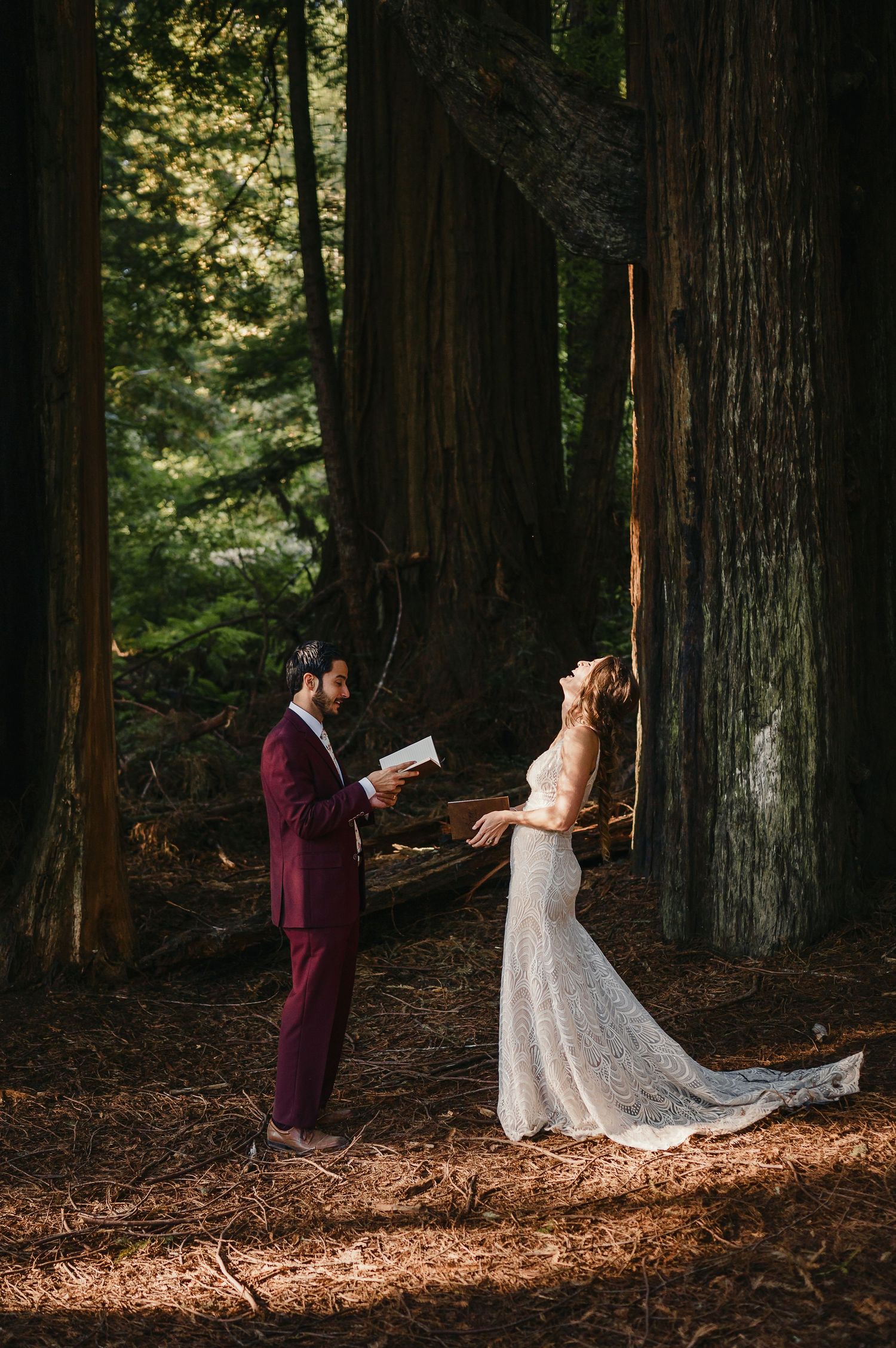 A wedding ceremony takes place among towering redwoods as the couple reads from books in the dappled sunlight.