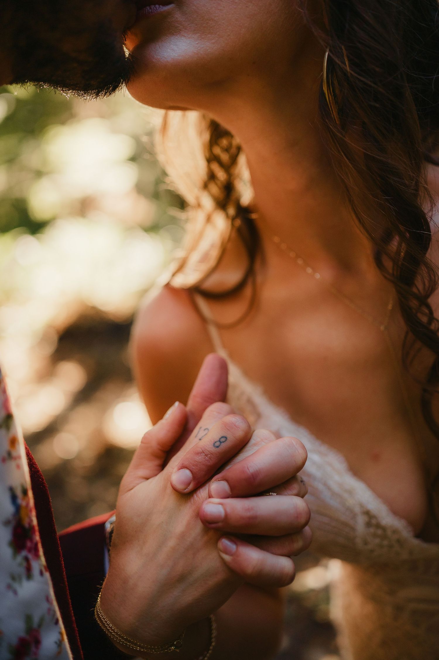 Close up detail of tender hands touching in dappled sunlight during an intimate forest moment.