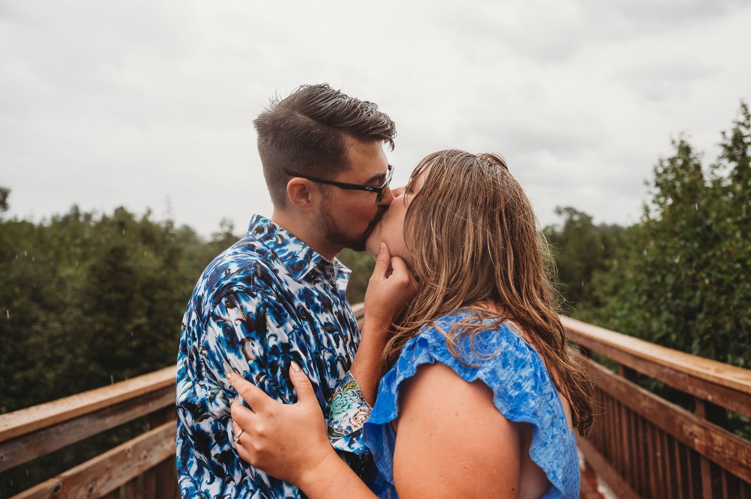 Couple in blue outfits share romantic moments on wooden boardwalk in outdoor nature setting.