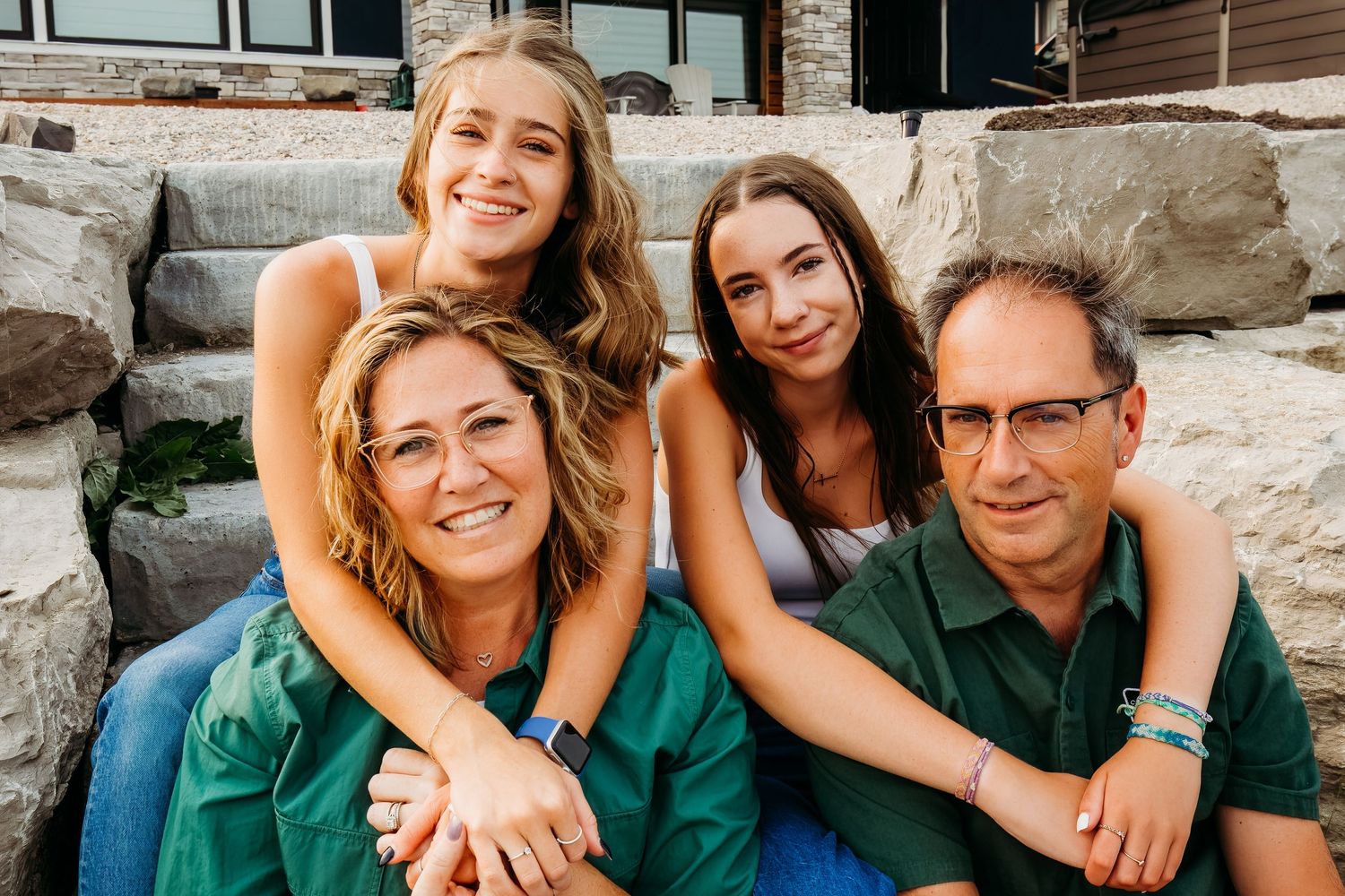 A group of four people in green clothing smile together while sitting on outdoor stone steps.