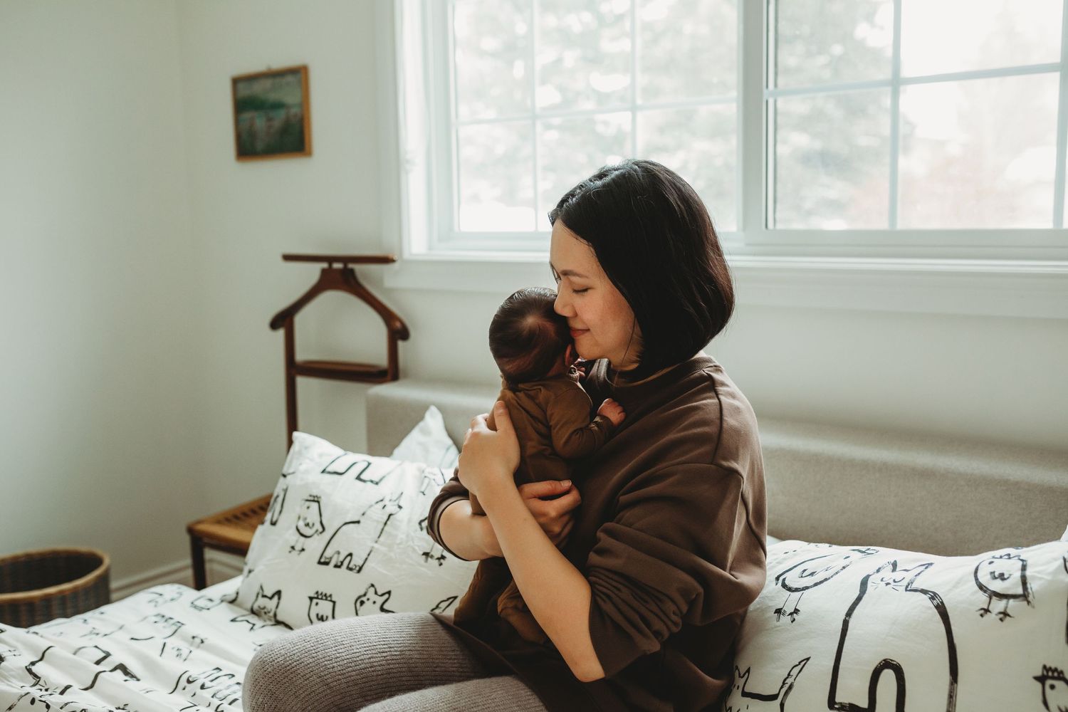 A moment of bonding on a white bed with patterned pillows in a sunlit room.