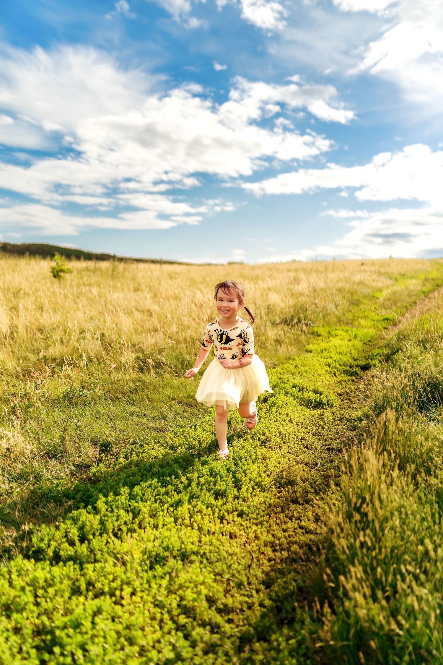 Young girl running through a summer field at Nose Hill Park, photographed by Calgary photographer Vendredi Phan of Doce Photography.
