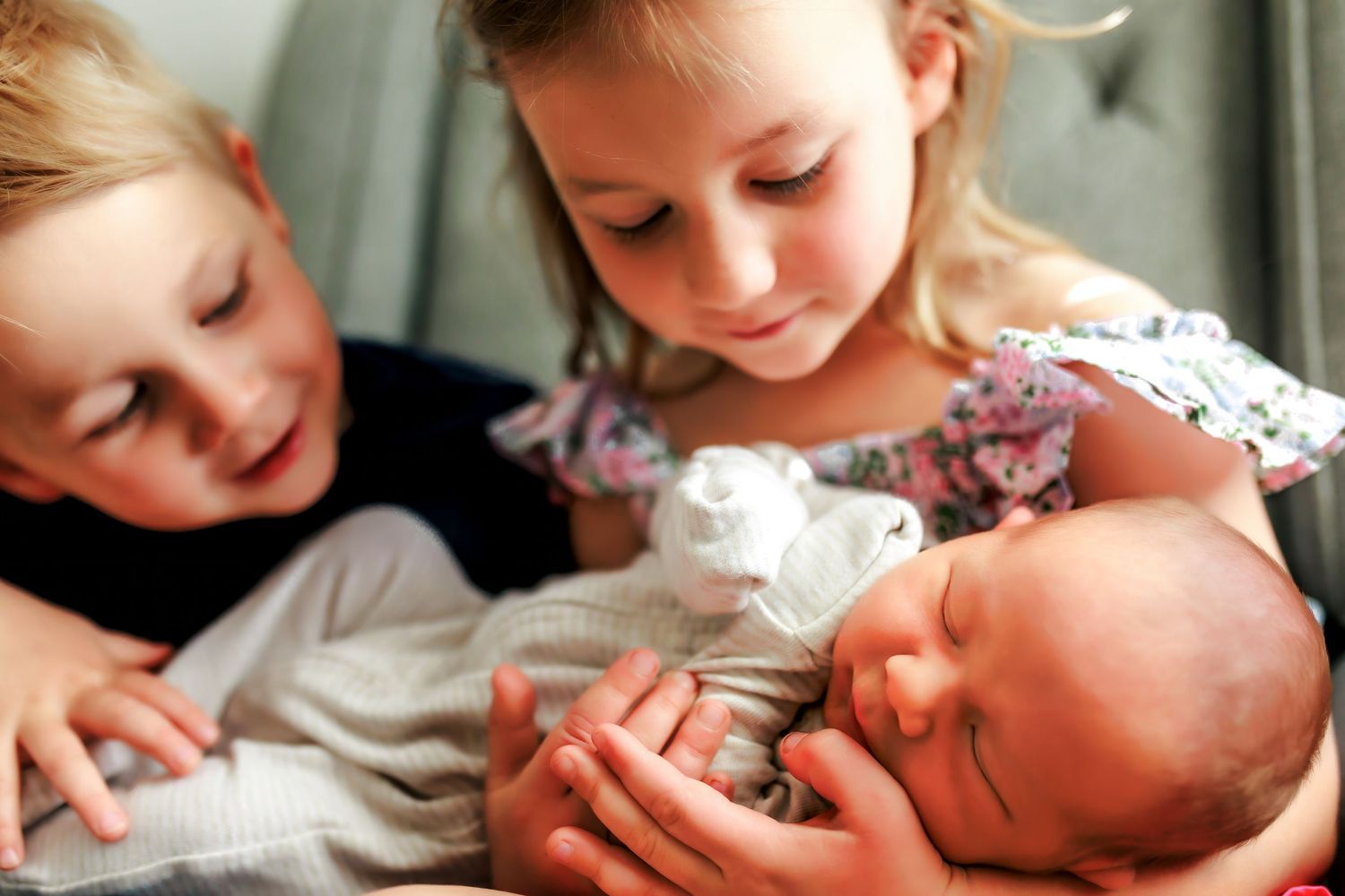 Sibling portraits in Calgary with kids gently holding their newborn baby during a lifestyle session.