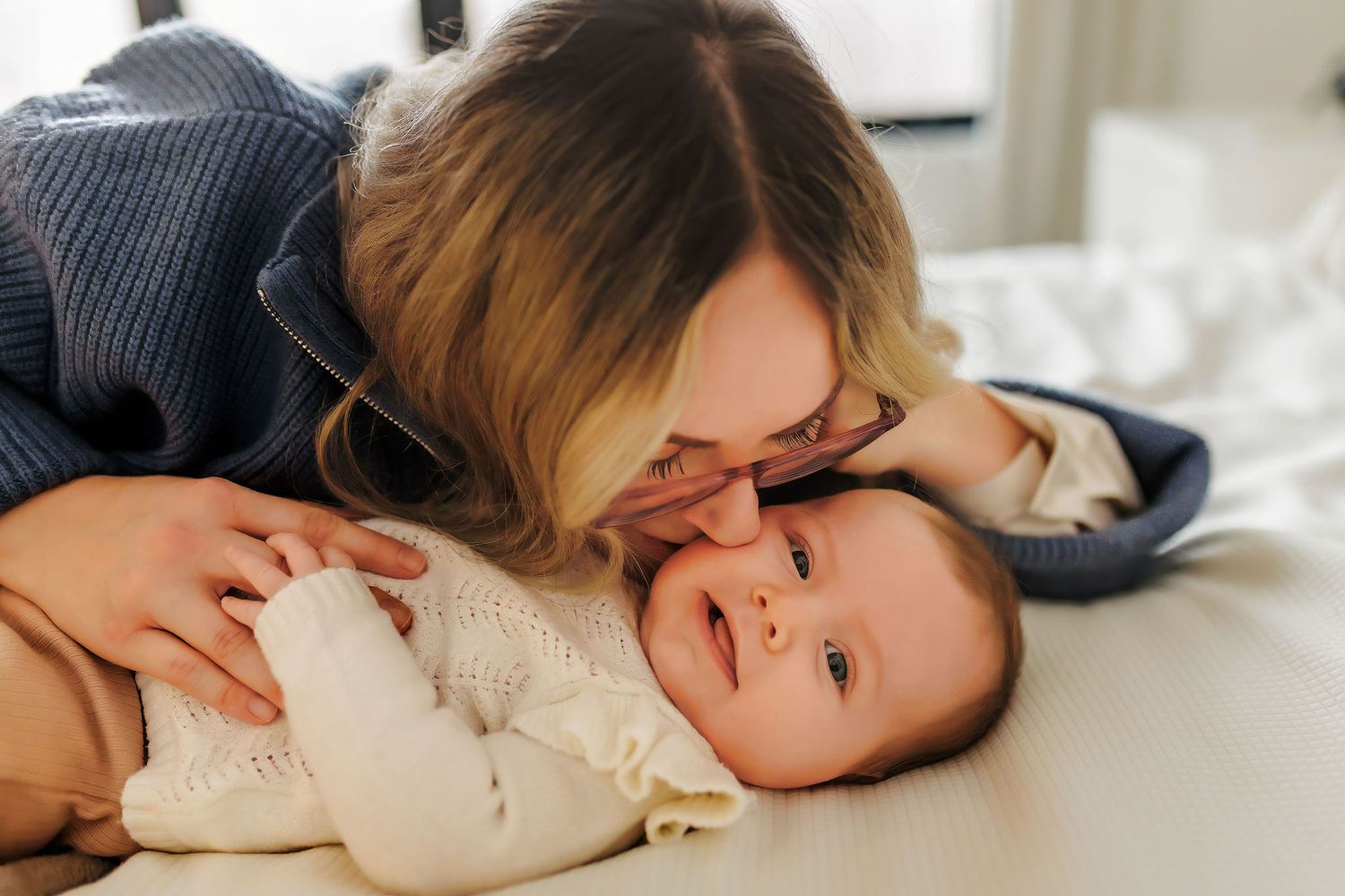 A warm bonding moment between a parent and infant lying on white bedding together.