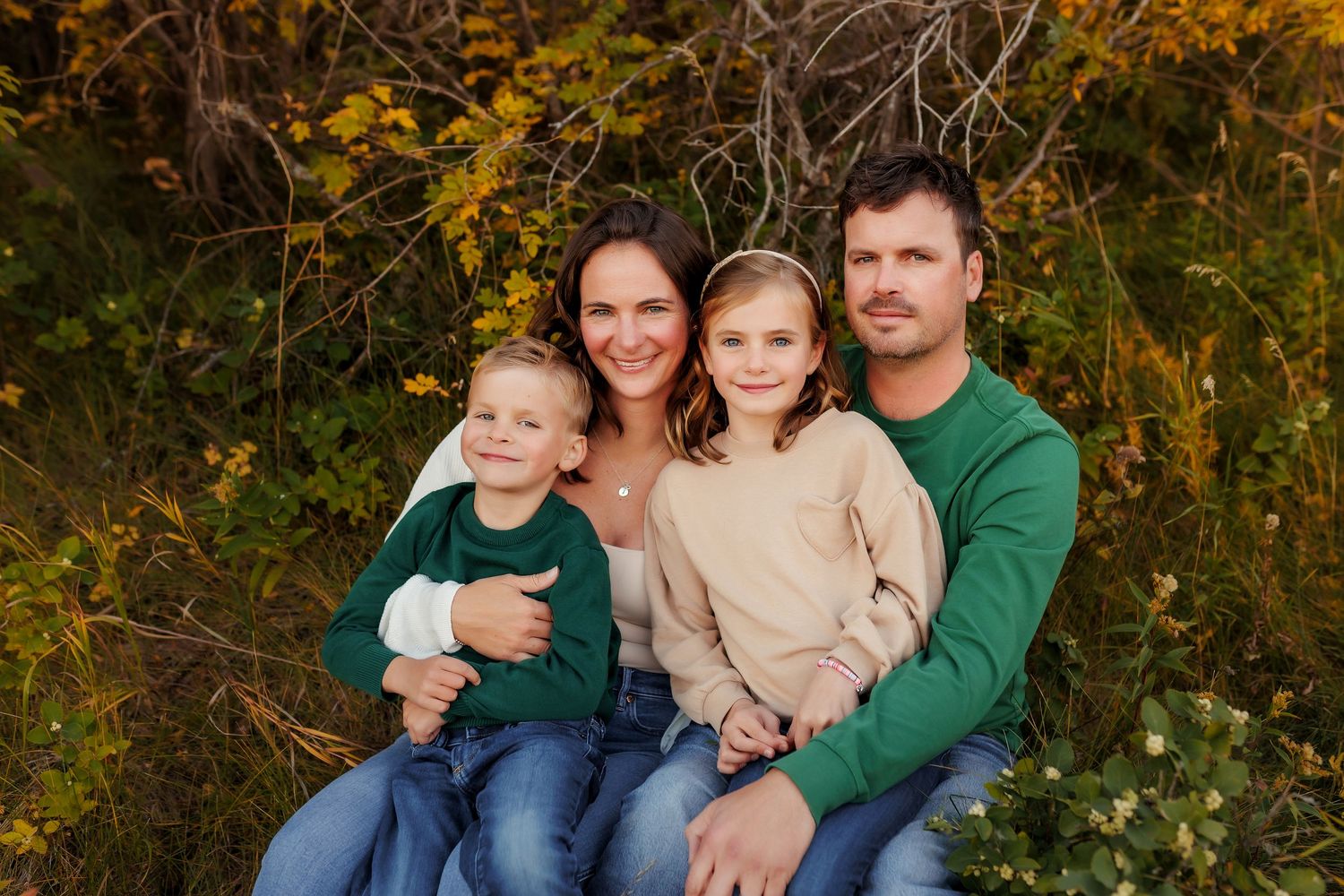 Family of four cuddling together during a fall photo session at Nose Hill Park in Calgary, Alberta.