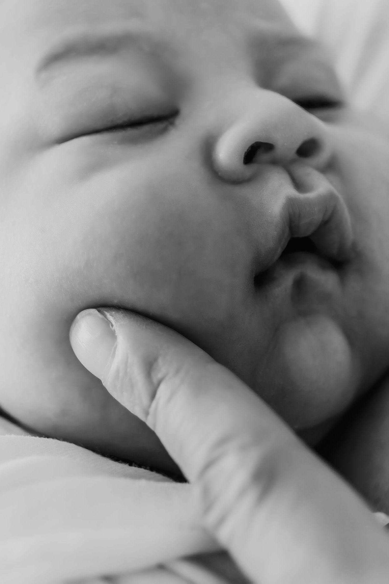 A close-up black and white photograph shows a sleeping baby with a finger gently pressed against their lips.