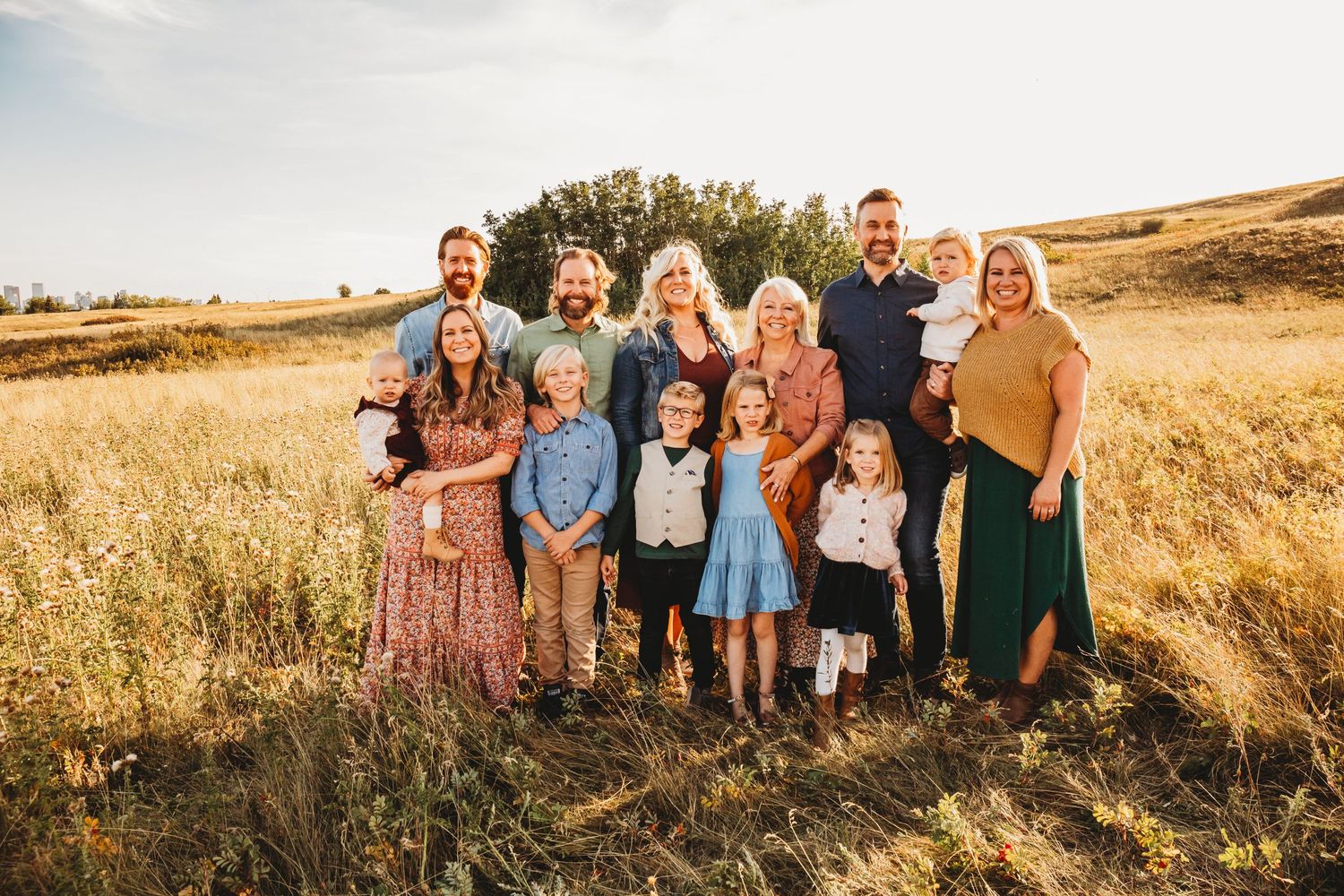 Group portrait of people in coordinated fall outfits standing together in a golden sunlit field at sunset.