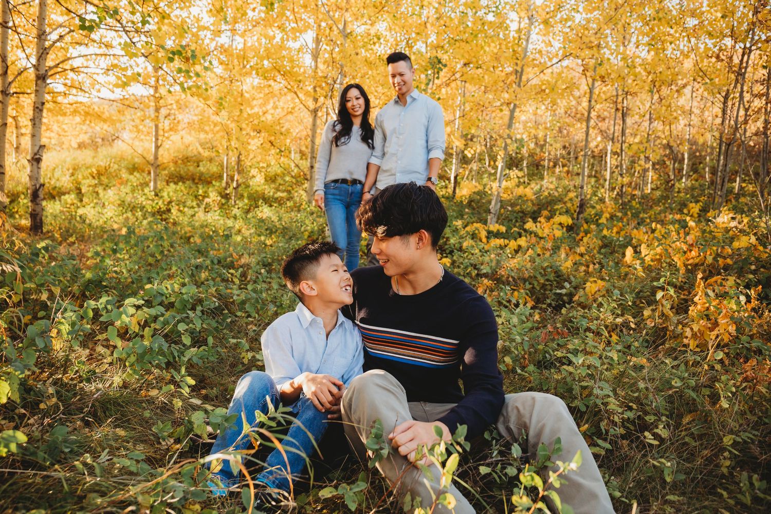 Family enjoying autumn scenery in a golden forest during sunset with yellow aspen trees and fallen leaves.