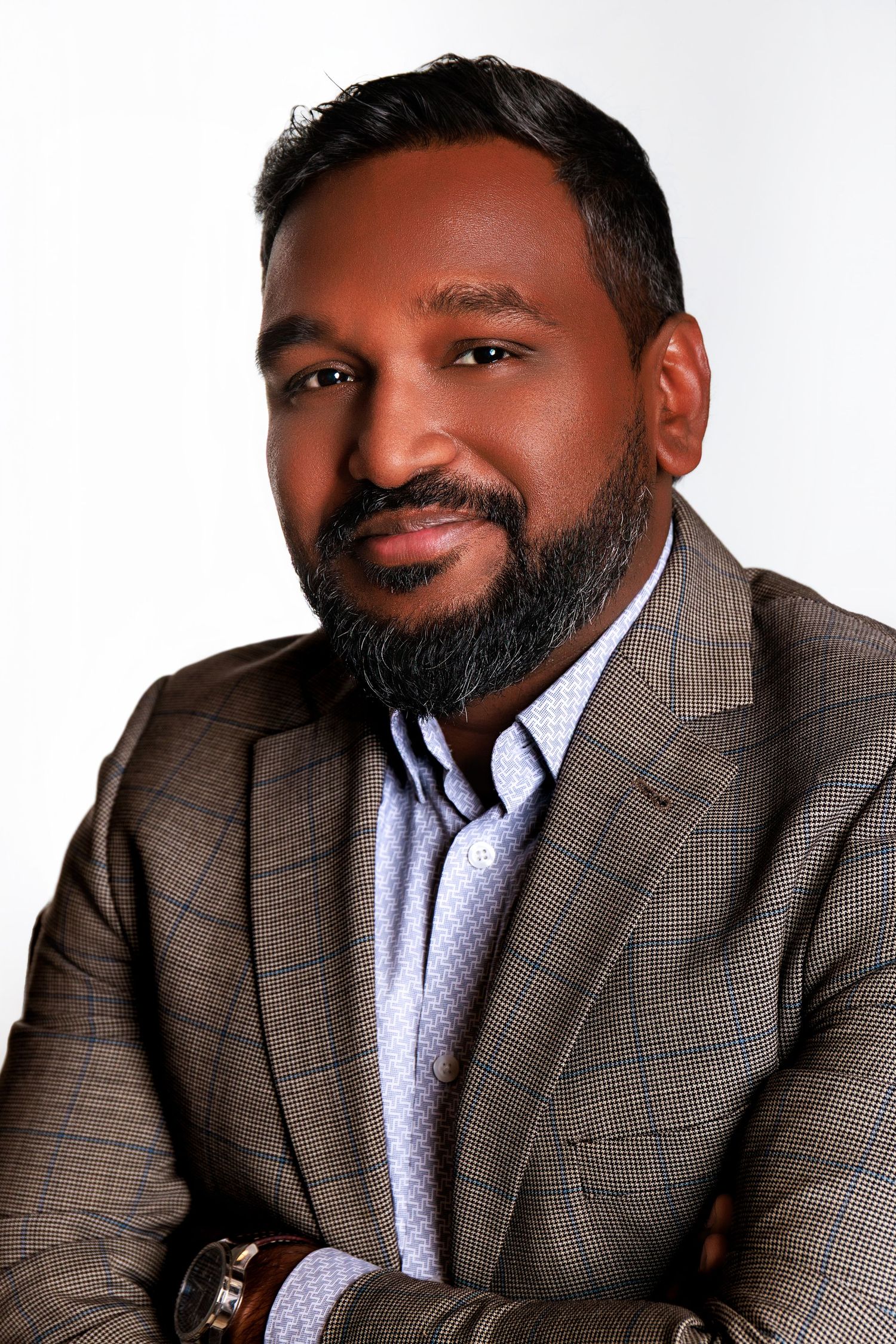 Professional headshot of someone wearing a plaid suit jacket and light blue button-up shirt against a white background.