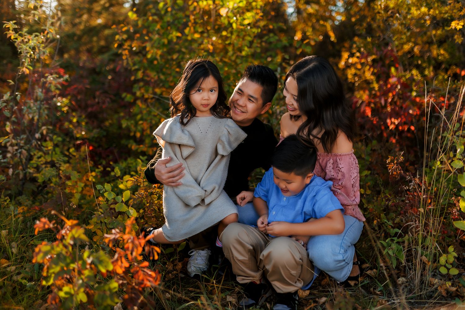 A family poses together outdoors surrounded by vibrant autumn foliage with golden and red leaves in the background.