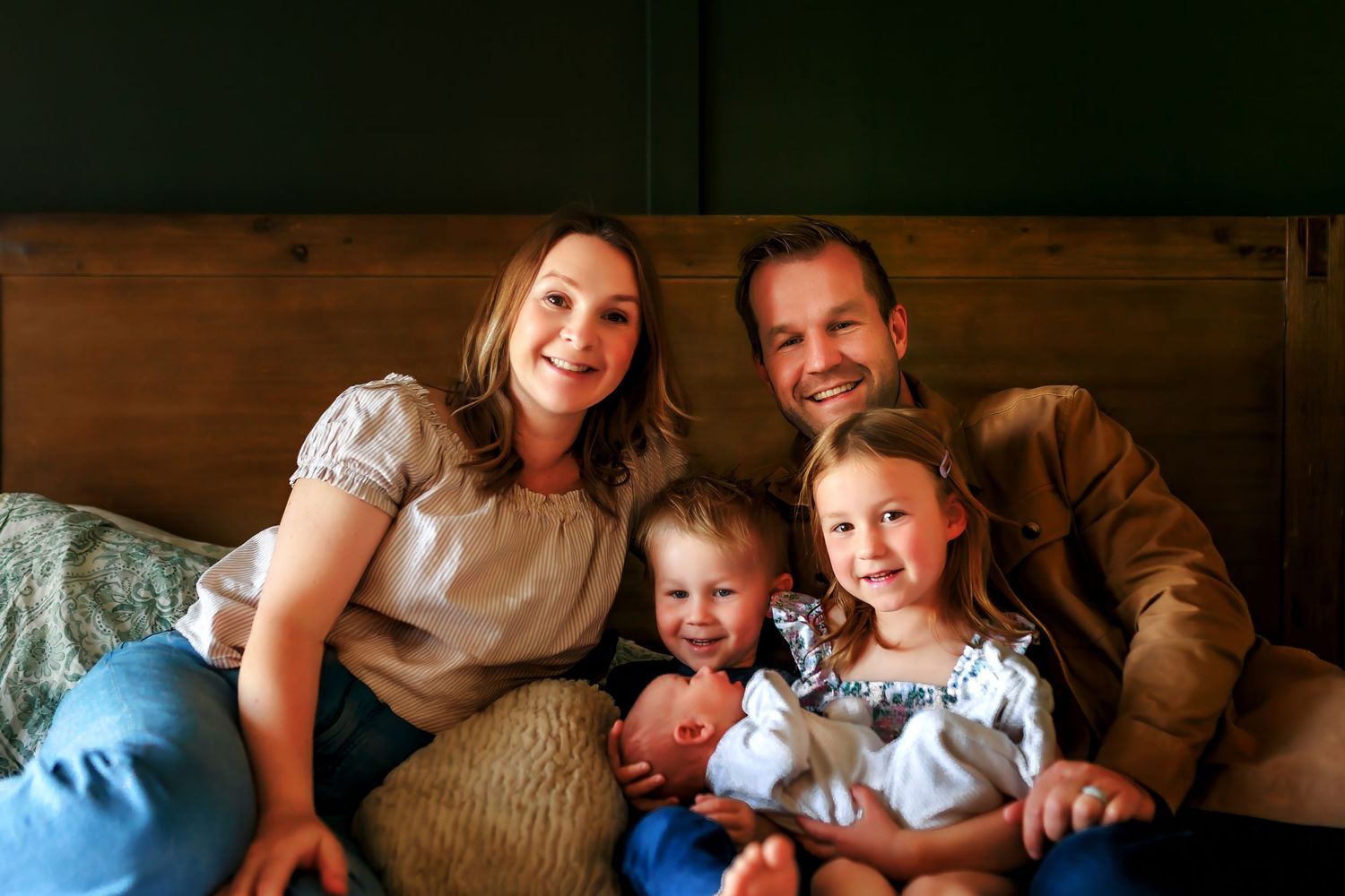 Lifestyle in-home newborn photography with family of four smiling together on the bed in Calgary.