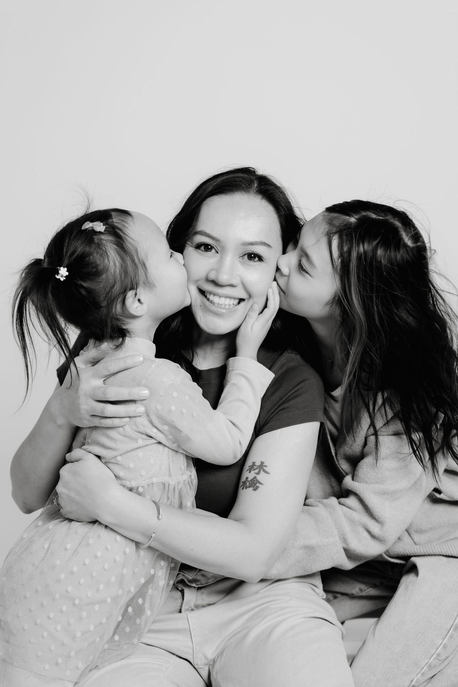 Black and white family portrait by Calgary photographer Vendredi Phan of Doce Photography showing joyful affection and kisses.