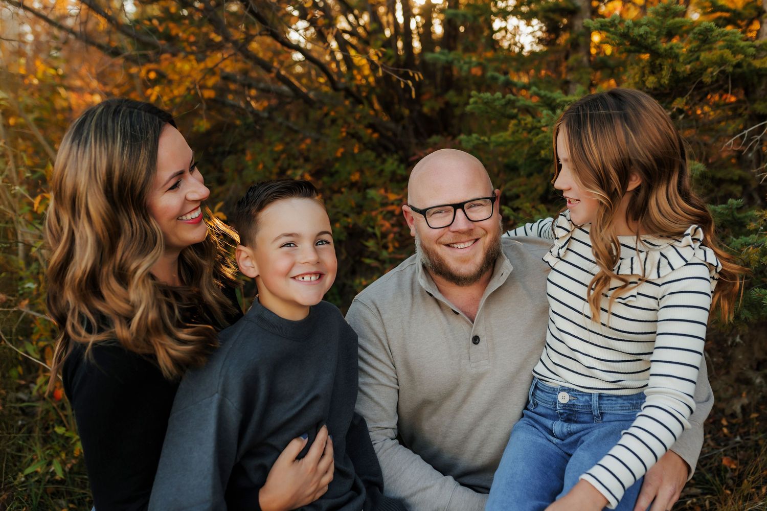 Happy family sharing laughter together during autumn photo session in front of fall foliage.