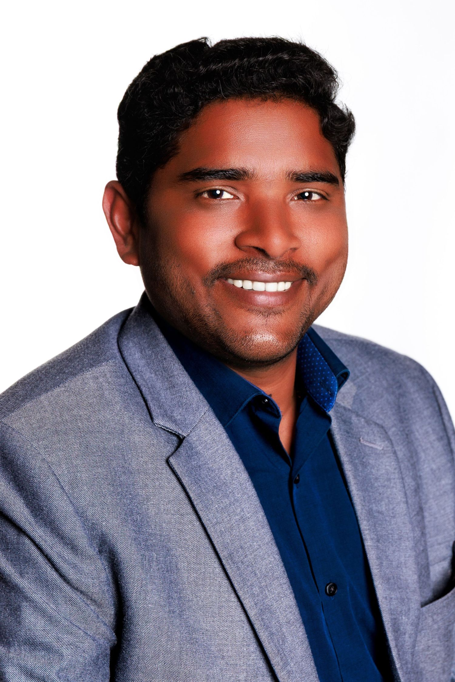 Professional headshot of person wearing a navy blue shirt and gray suit jacket against white background.