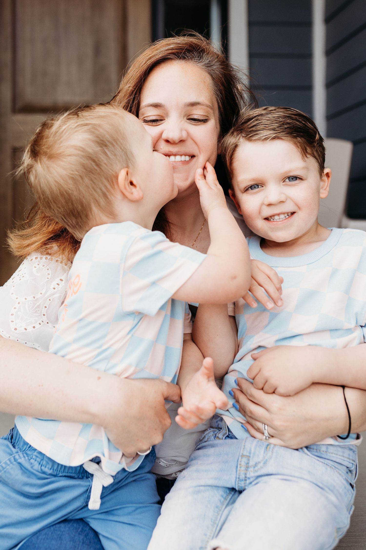 Sweet family moment captured outdoors showing affectionate interaction and joyful smiles in matching light blue outfits.