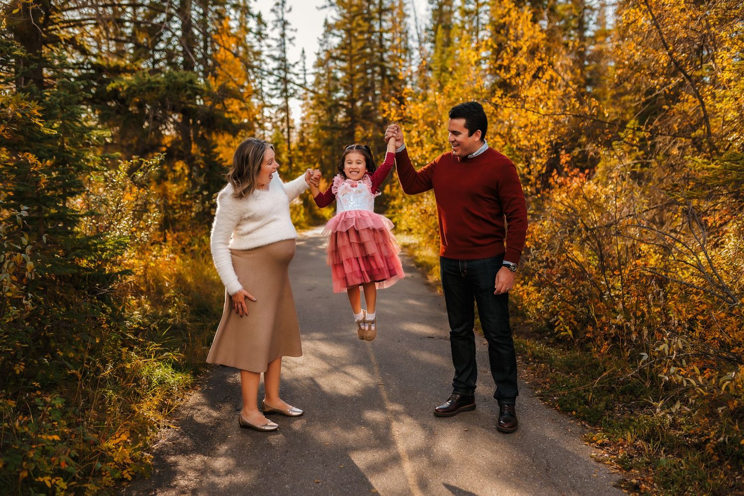 Family plays together on a forest path surrounded by vibrant yellow autumn foliage in the wilderness.