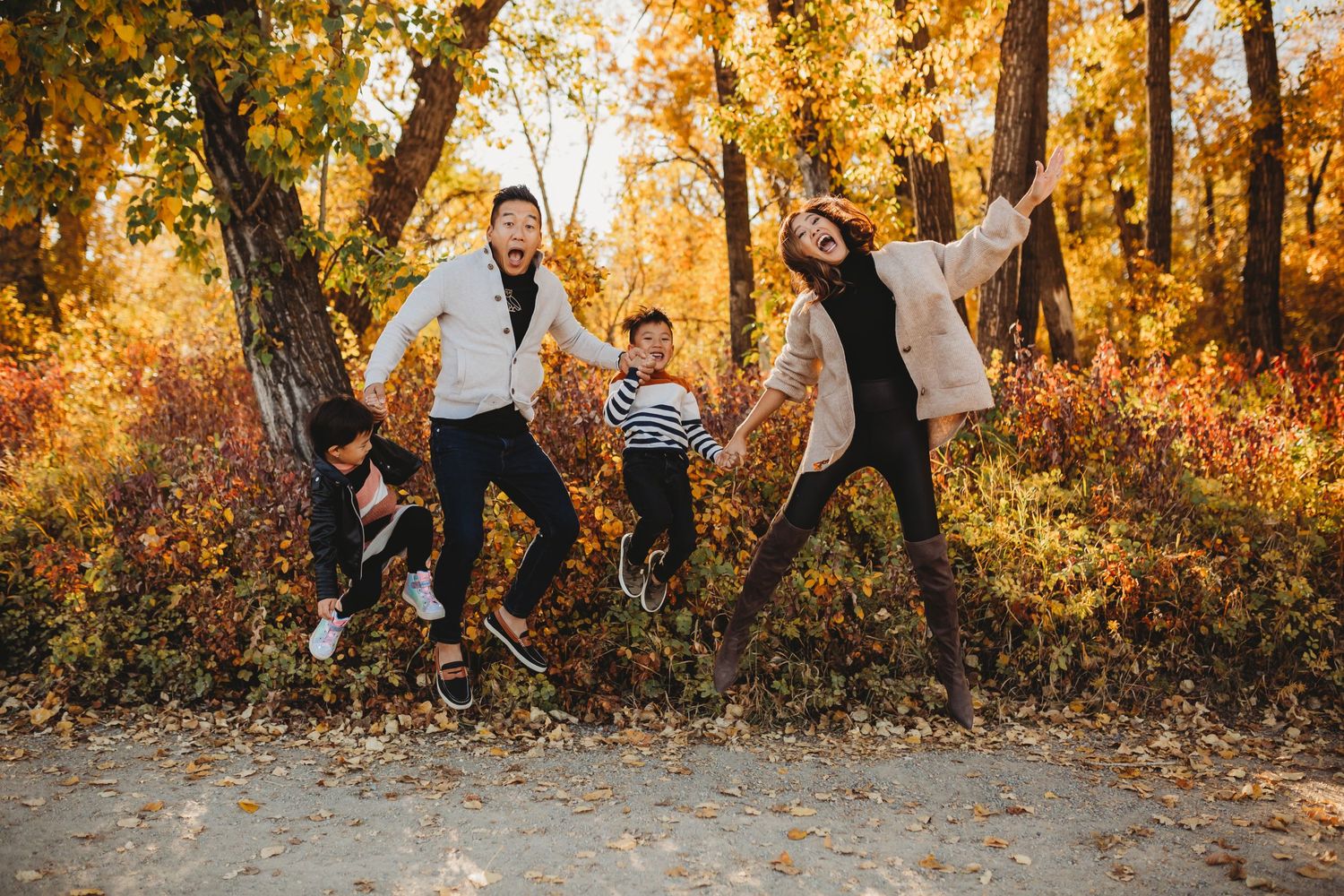 People jumping joyfully on a path surrounded by vibrant golden autumn trees and foliage in a park setting.