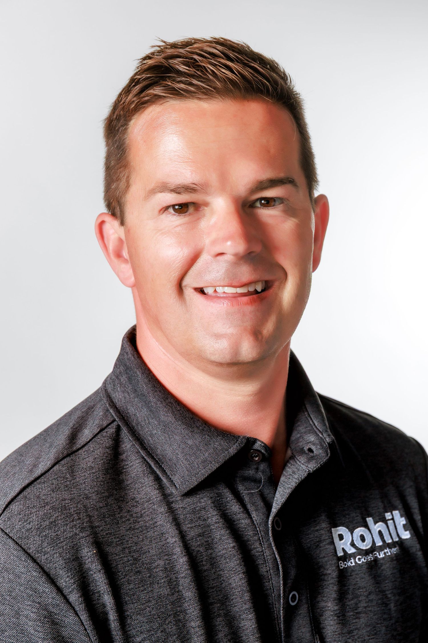 Professional headshot of someone wearing a dark gray polo shirt with Rohit company logo against white background.