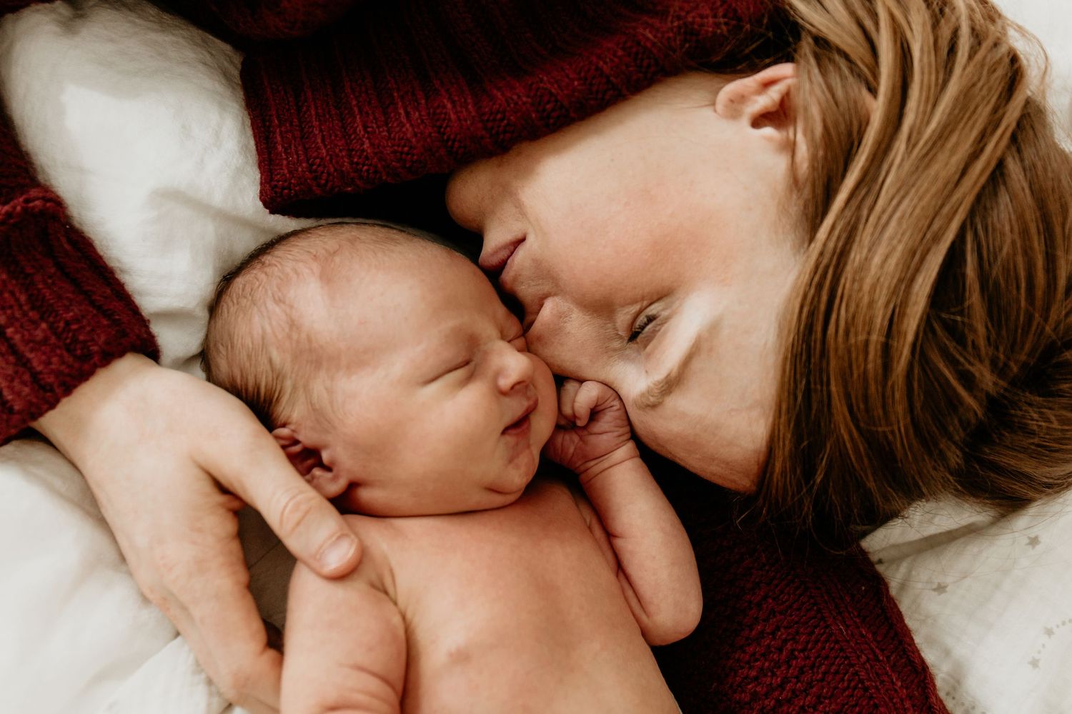A tender moment shows close physical connection between parent and newborn baby resting on burgundy fabric.