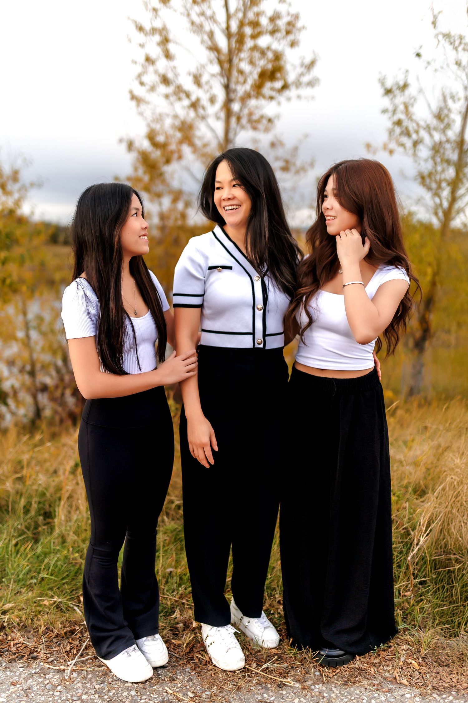 Three friends in casual outfits enjoying a warm autumn day outdoors in a field with golden grass and trees.