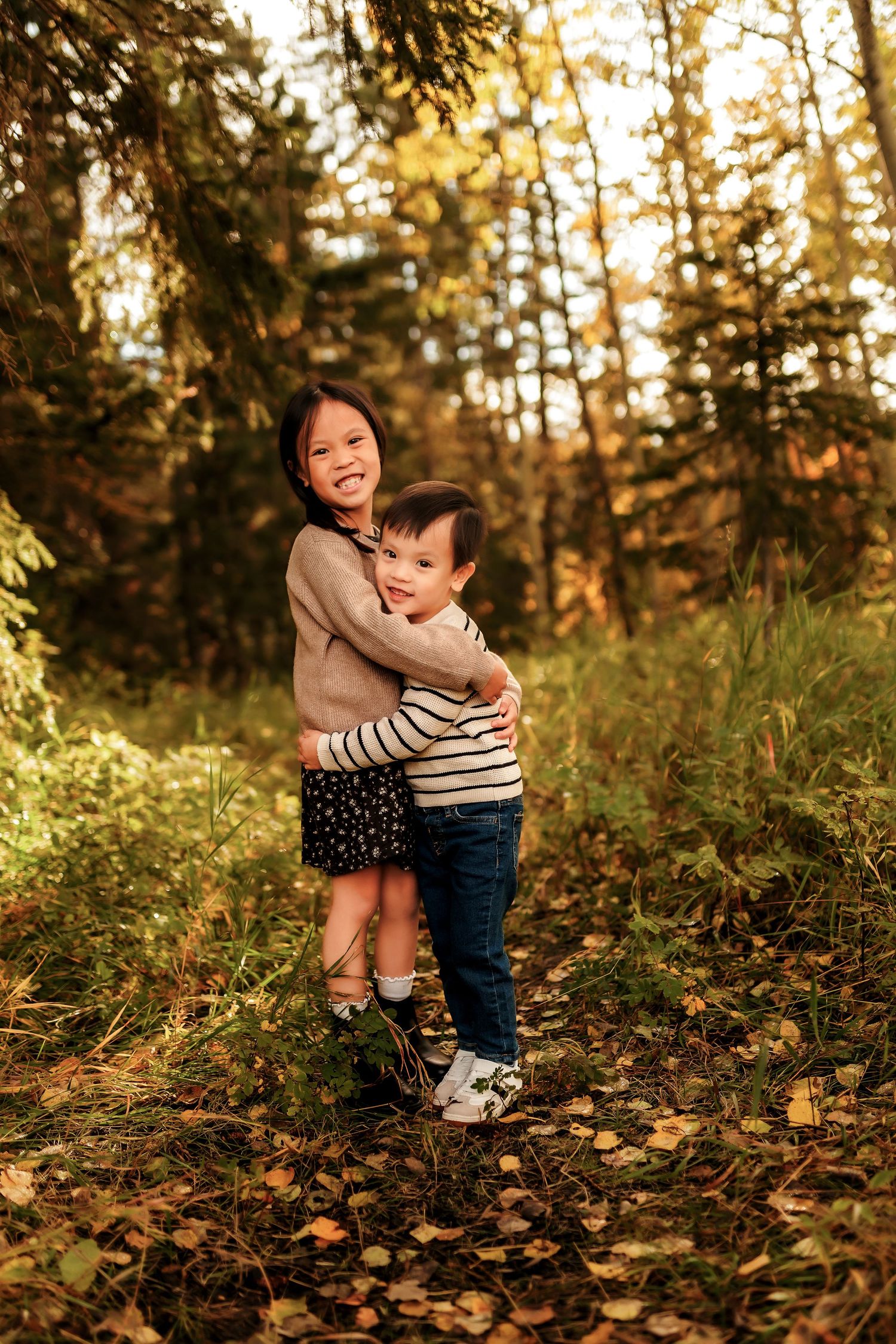 Brother and sister hugging and smiling at the camera during a fall family photography session at Shannon Terrace Park in Calgary.