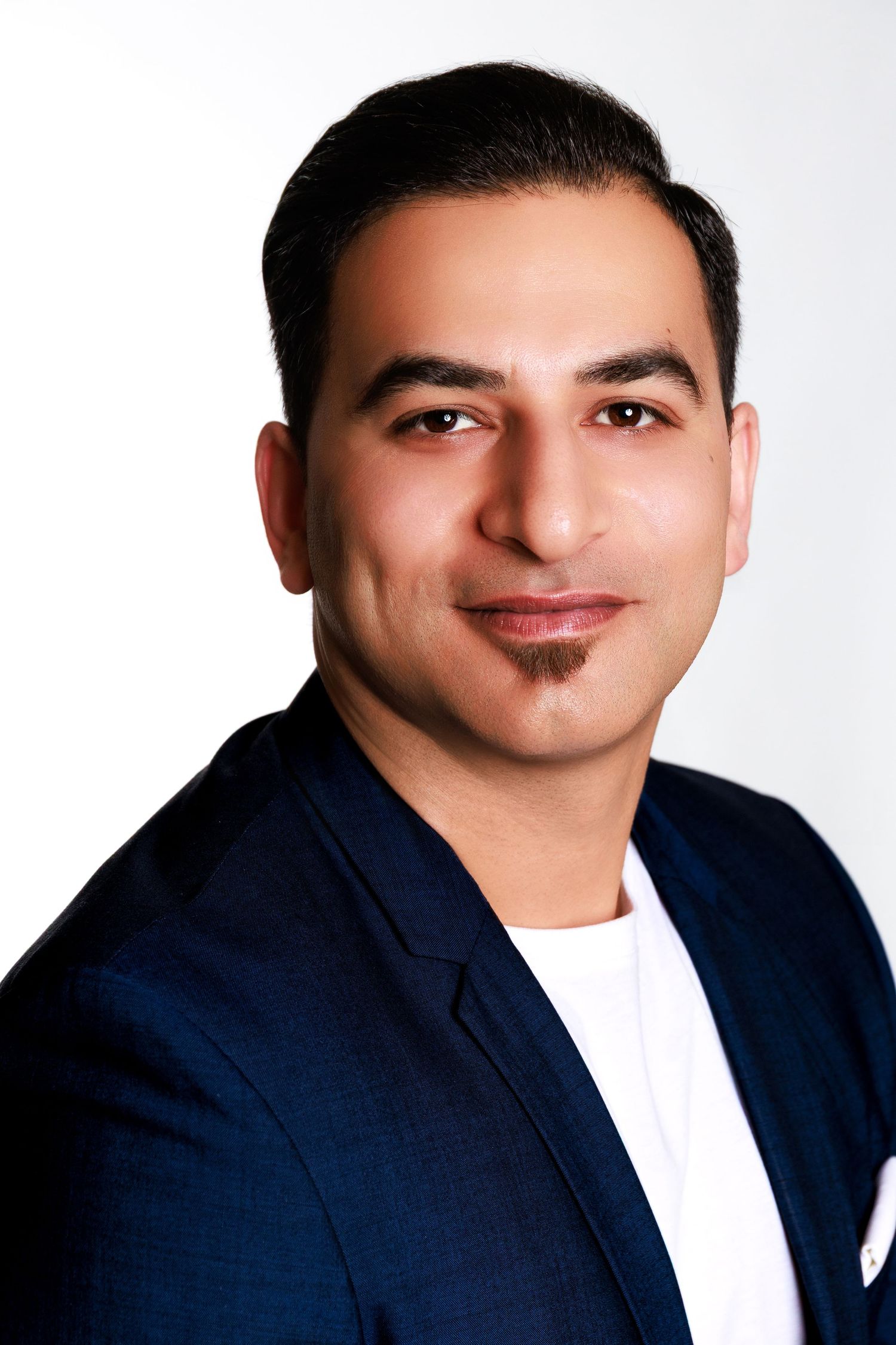 Professional headshot portrait of someone in a navy blazer and white t-shirt against a light background.
