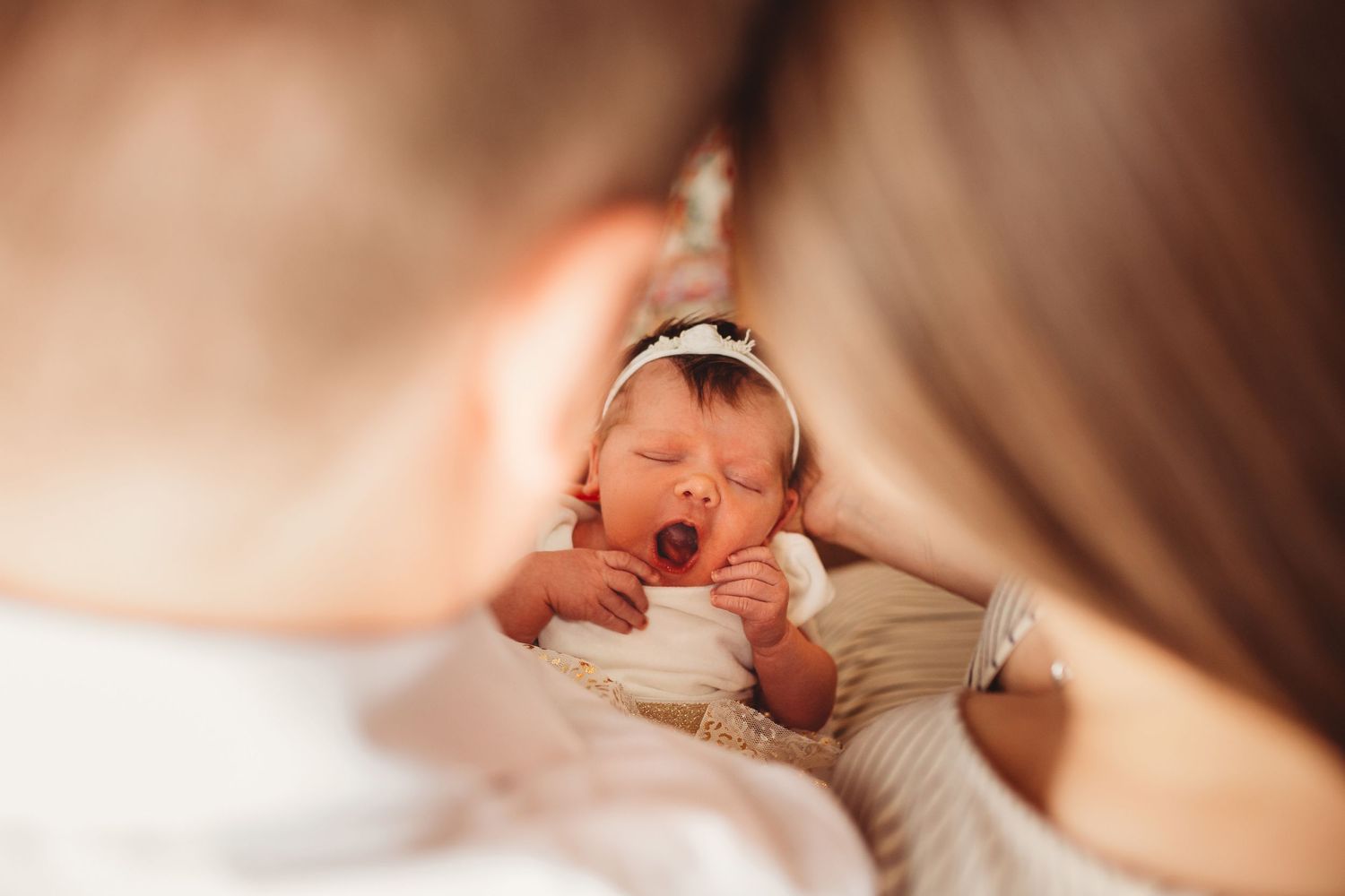 A newborn baby yawns while swaddled in a soft white blanket during a portrait session.