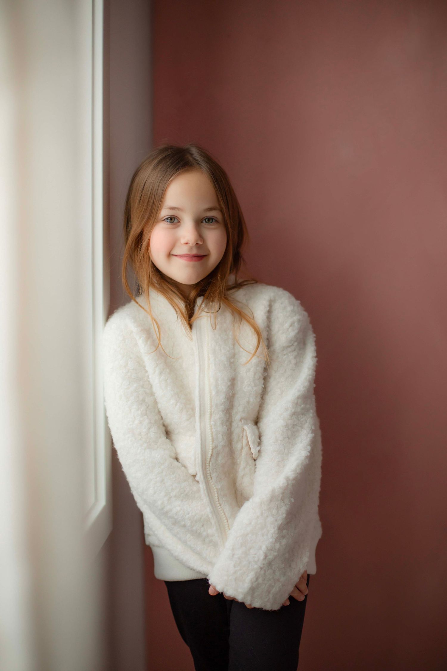 A sequence of casual portrait poses wearing a cozy white winter jacket against a burgundy wall.