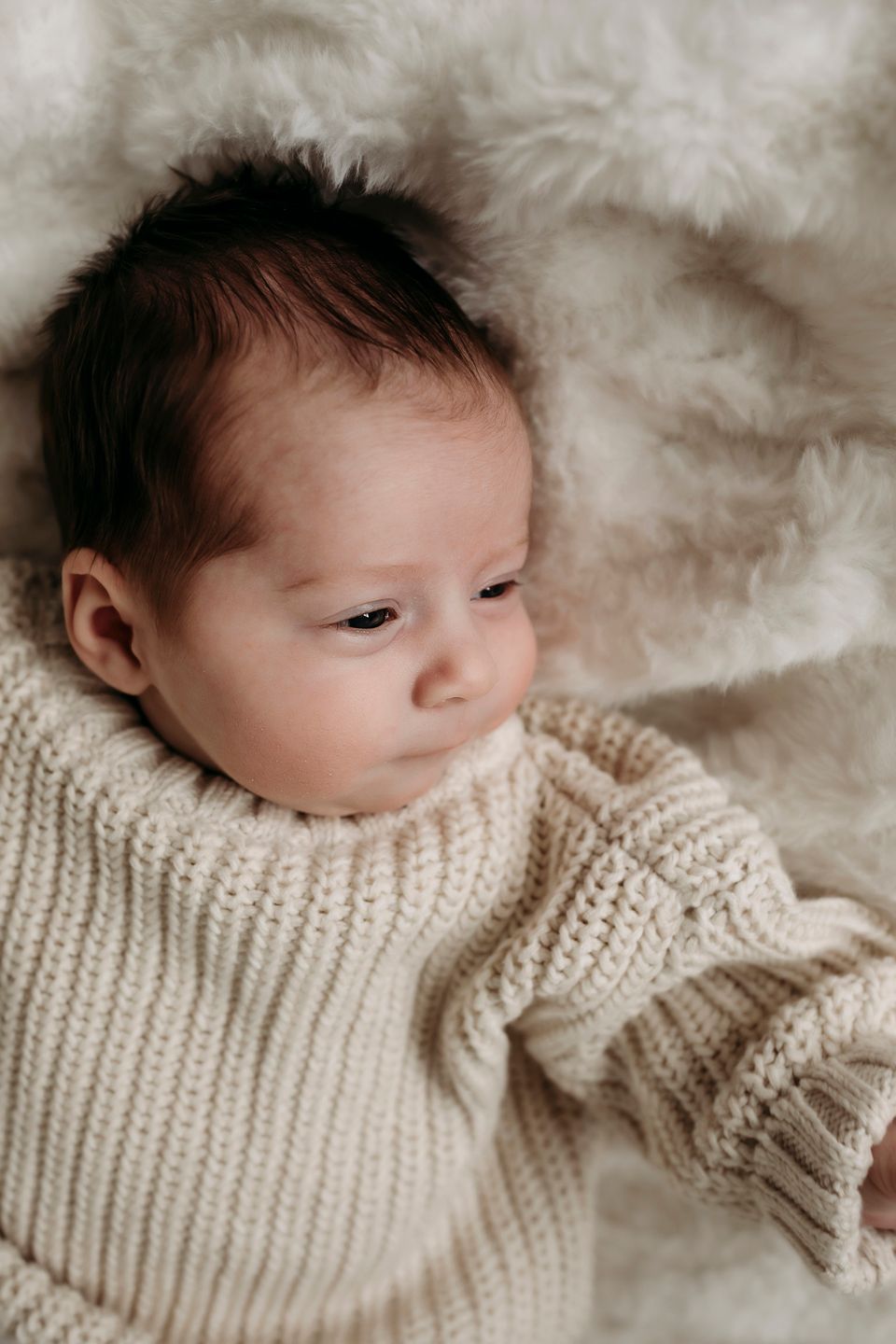 Baby wearing cozy cream knit sweater lying on soft white blanket.