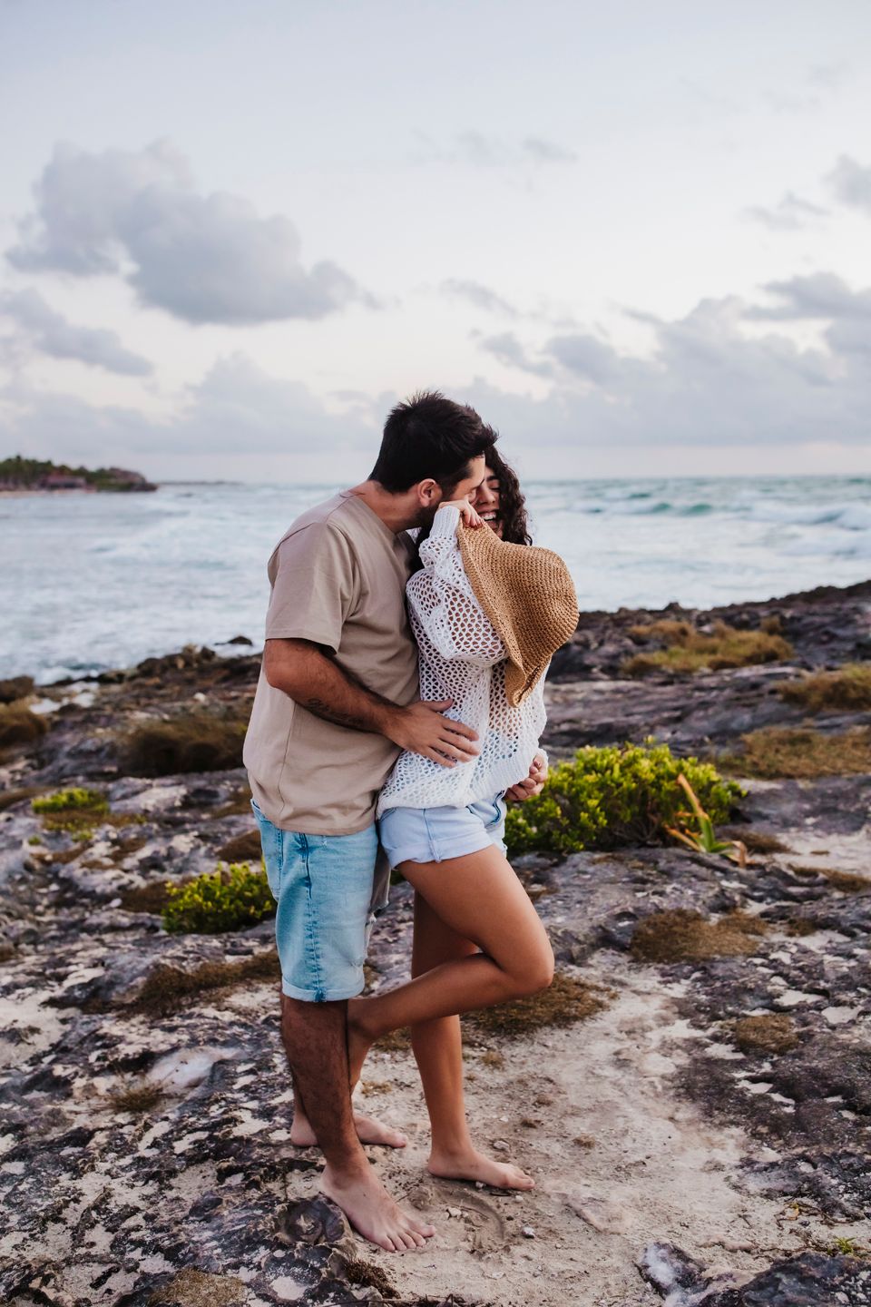 Couple sharing intimate moment on rocky coastline with ocean view.