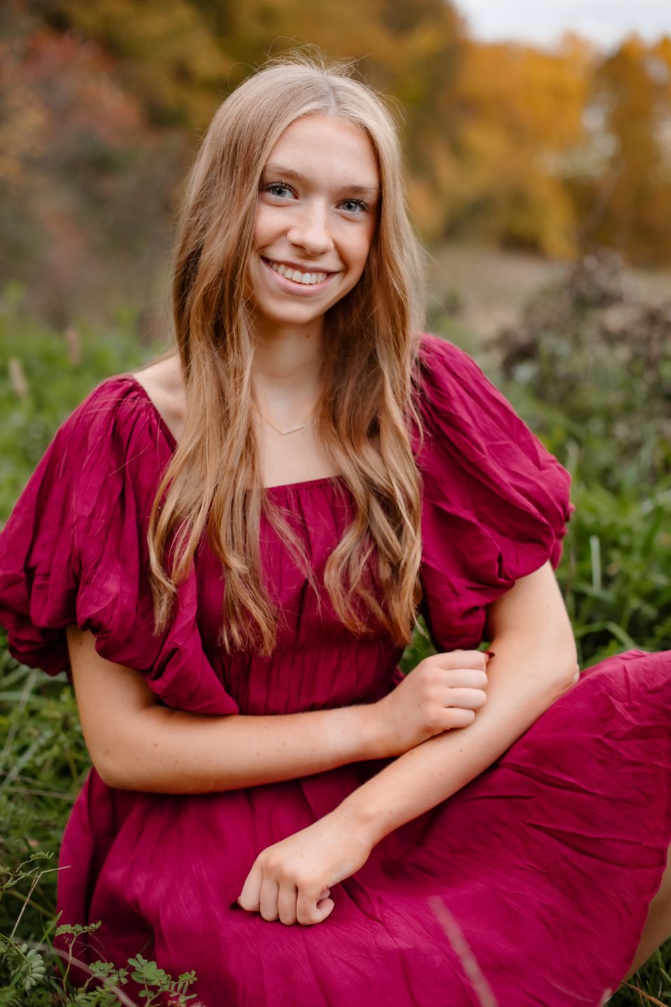 Portrait featuring burgundy dress with puff sleeves against vibrant fall foliage background.