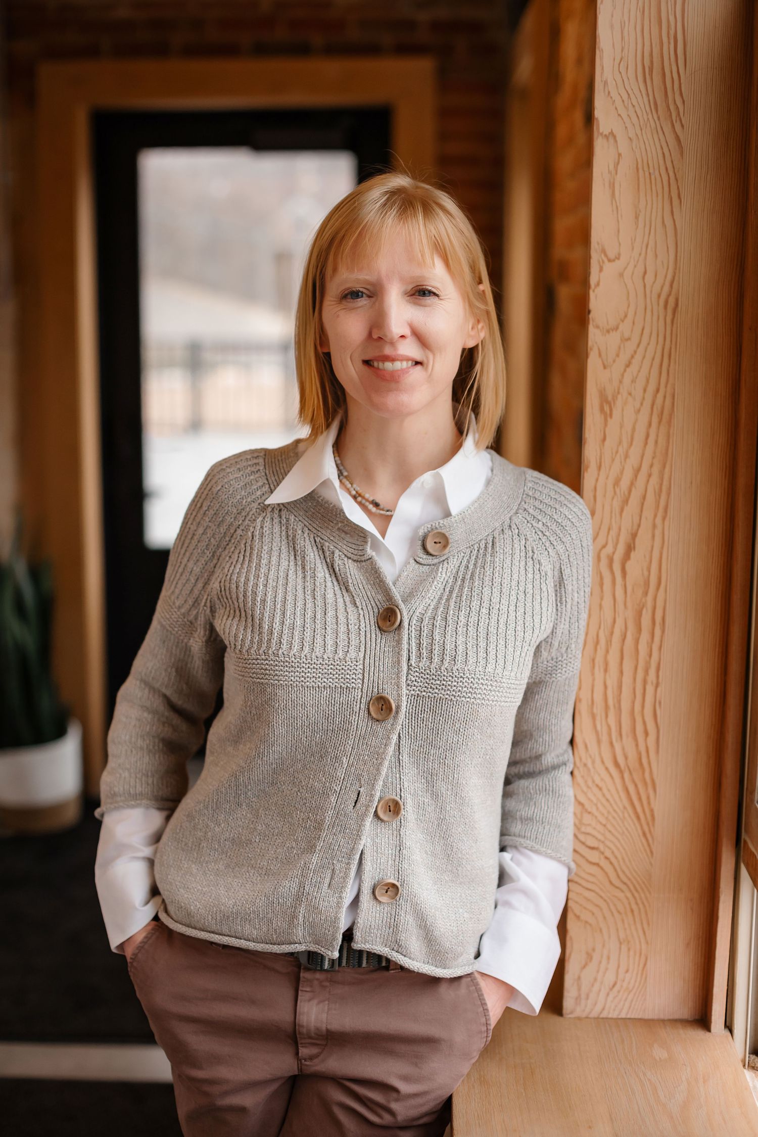 Professional portrait in wooden-framed doorway wearing gray cardigan and white shirt.