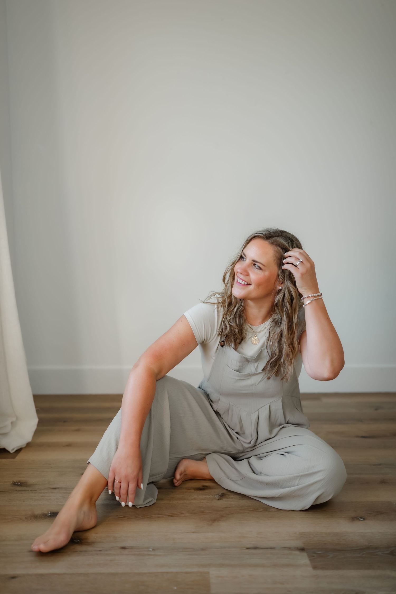 Relaxed candid portrait of someone sitting on floor in gray outfit by window.