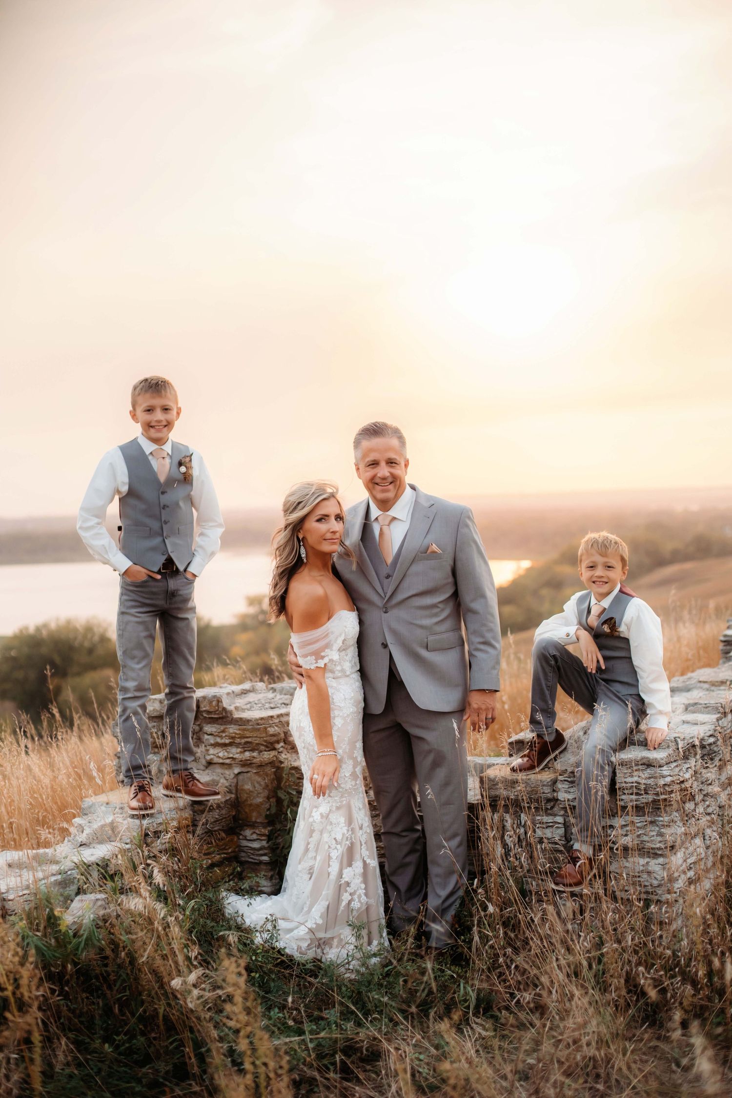 Family wedding portrait with children standing on stone wall during golden hour.